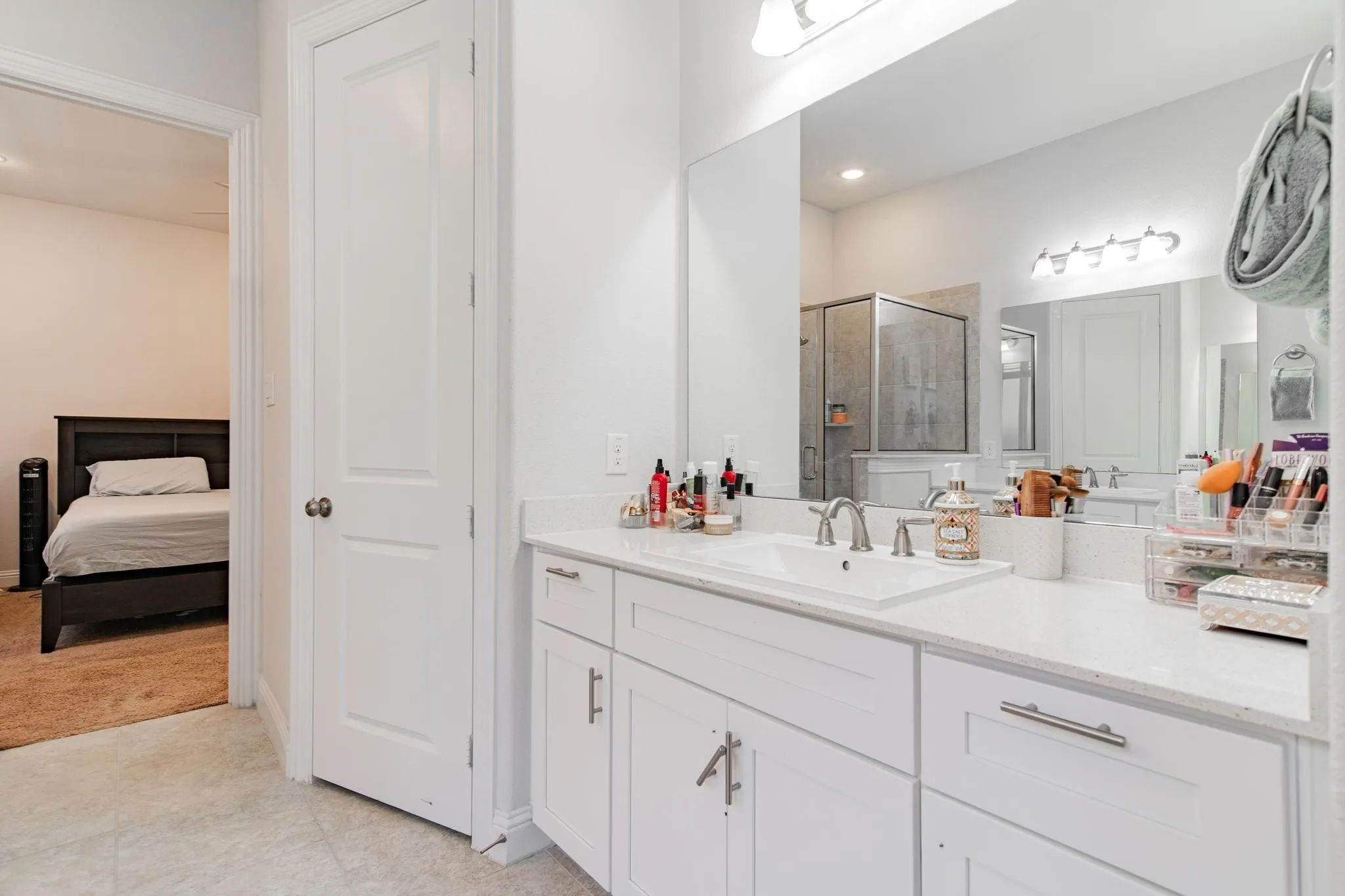 White vanity with integrated sink, brushed nickel faucet, large vanity mirror, glass-enclosed shower, and tile flooring