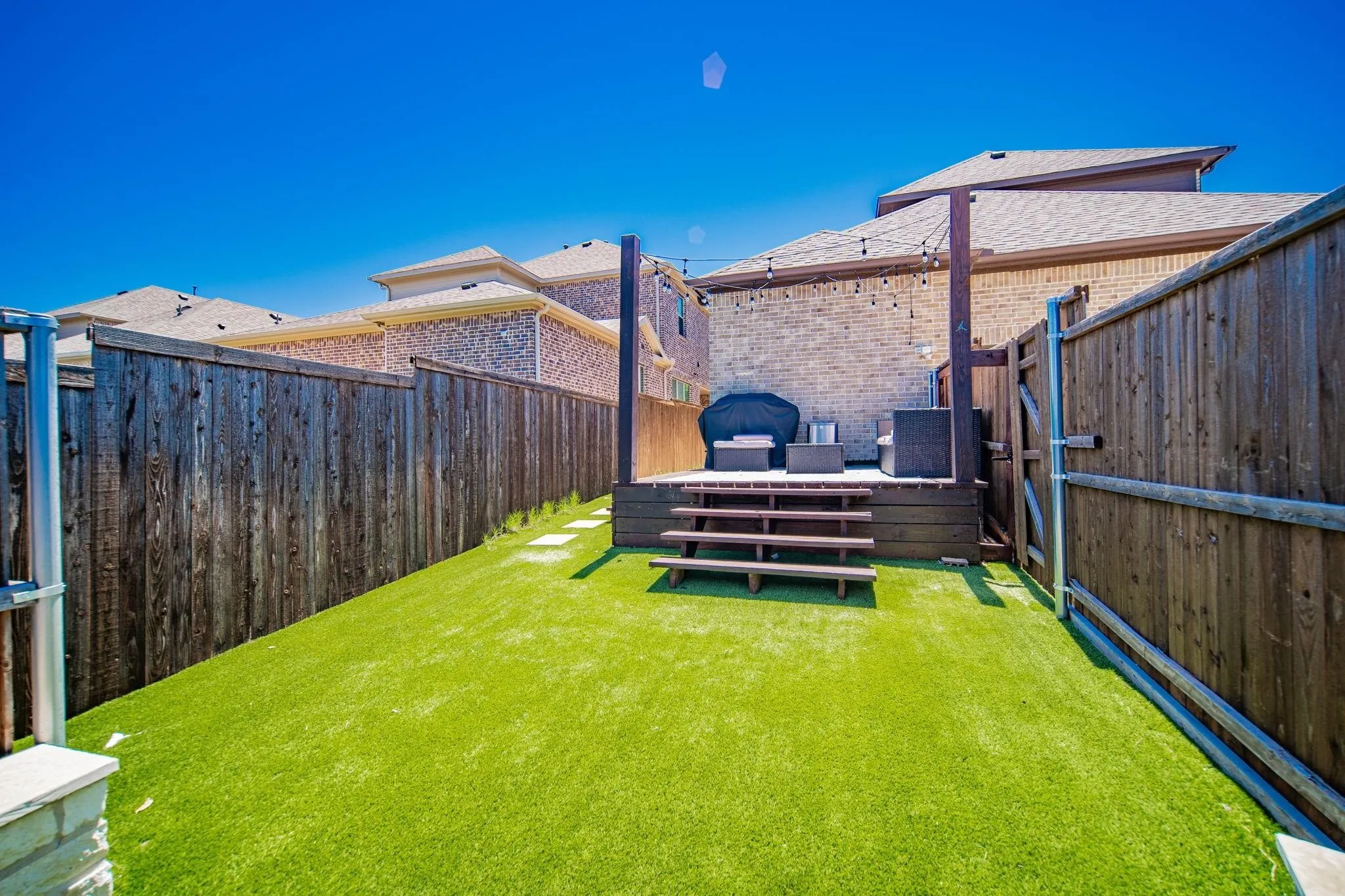 Backyard featuring artificial turf, a wood-finish deck with steps, string lighting, and wood privacy fencing