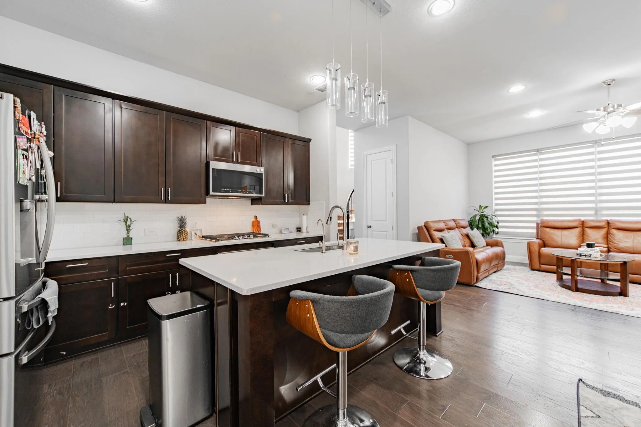 Kitchen island with white countertop, dark wood-finish cabinetry, stainless steel appliances, and wood-finish flooring
