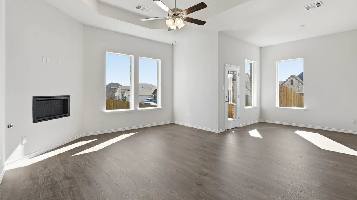 Bright, open living space showcasing wood-finish flooring, abundant natural light from multiple large windows, ceiling fan with integrated lighting, a fireplace with dark surround, and architectural details including glass-paneled interior doors with mountain backdrop views