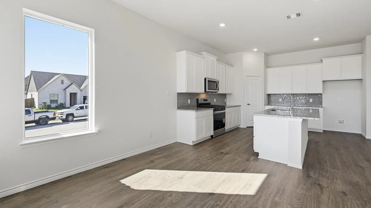 Open-concept living area featuring wood-finish flooring, white cabinetry, a kitchen island with an integrated sink, stainless steel appliances, and recessed lighting