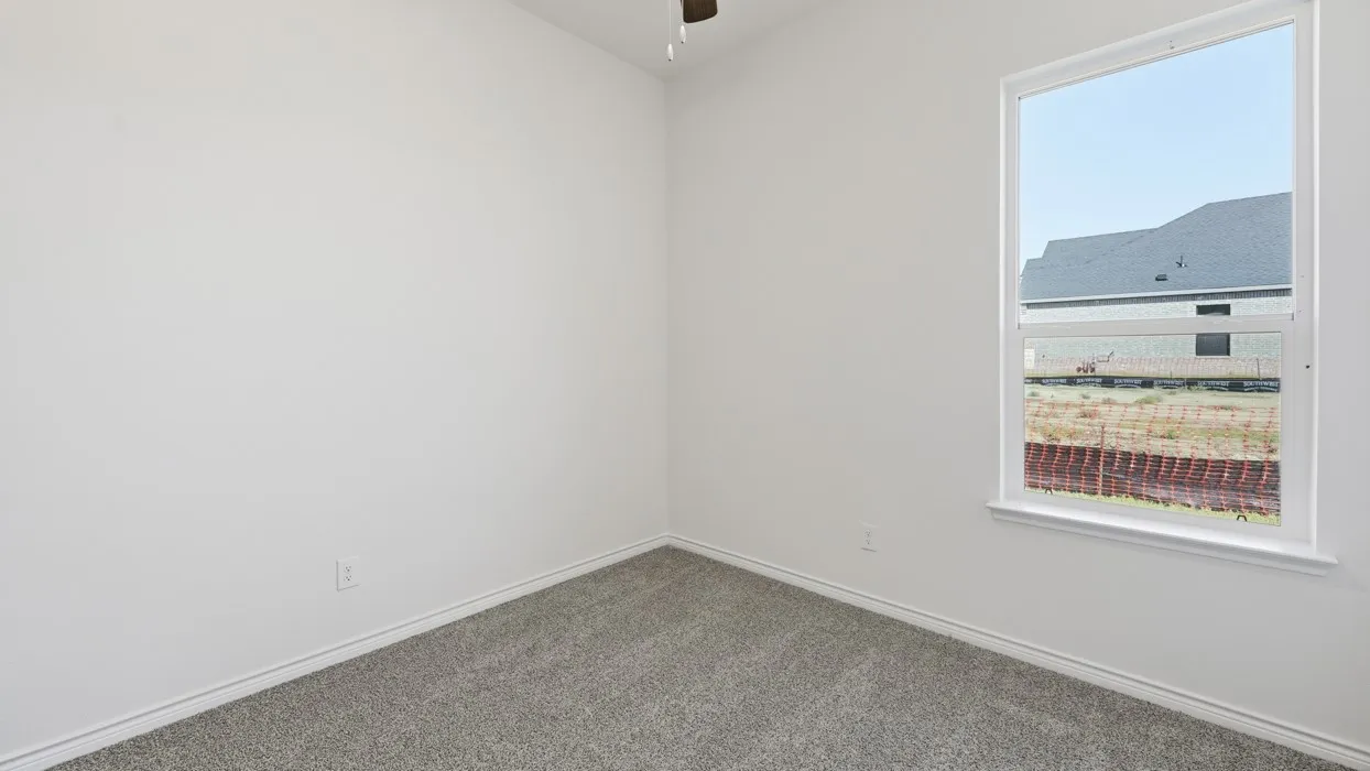 Bright corner bedroom with plush carpeting, clean white walls, and abundant natural light from an oversized window framing scenic neighborhood vistas