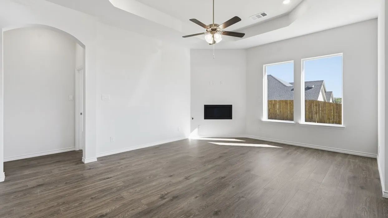 Bright and spacious room featuring wood-finish flooring, recessed ceiling detail with ceiling fan, large dual windows with natural light, and clean white walls throughout