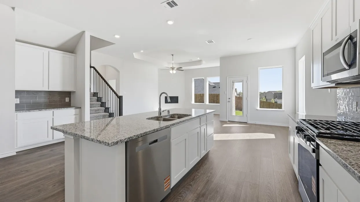 Expansive kitchen featuring white cabinetry, granite countertops, stainless steel appliances, and a central island with an undermount sink