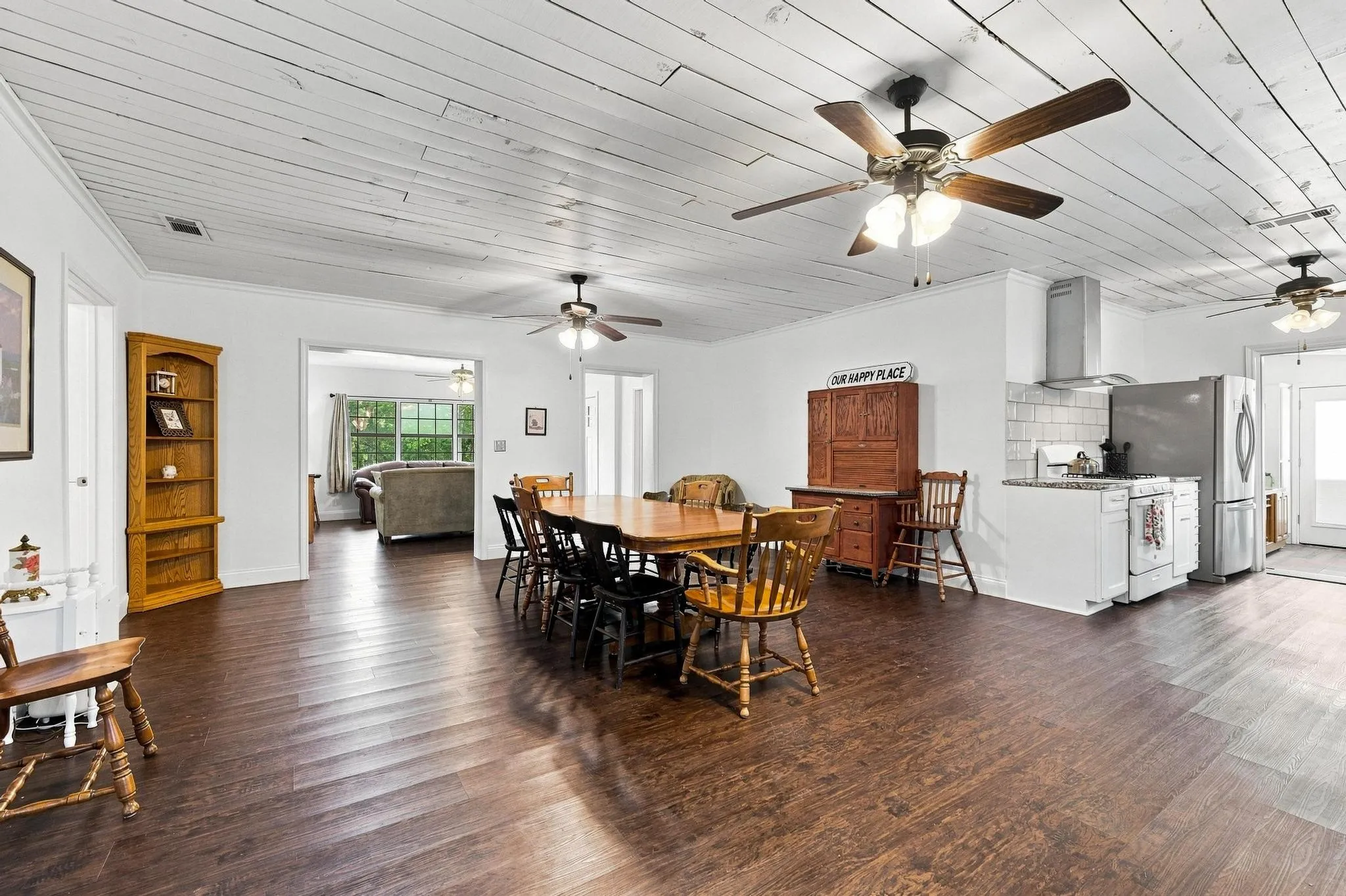 Wood-finish flooring throughout, white plank ceiling, multiple ceiling fans, kitchen area with stainless steel appliances, and built-in corner shelving