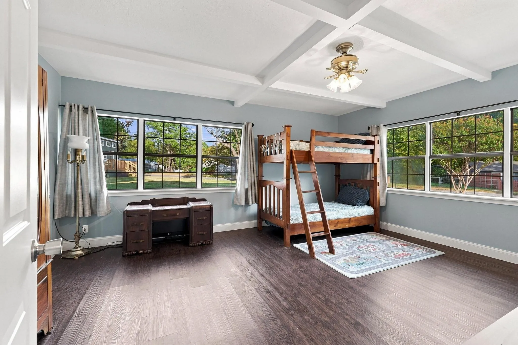 Spacious room featuring wood-finish flooring, abundant natural light, and a tray ceiling with a central light fixture