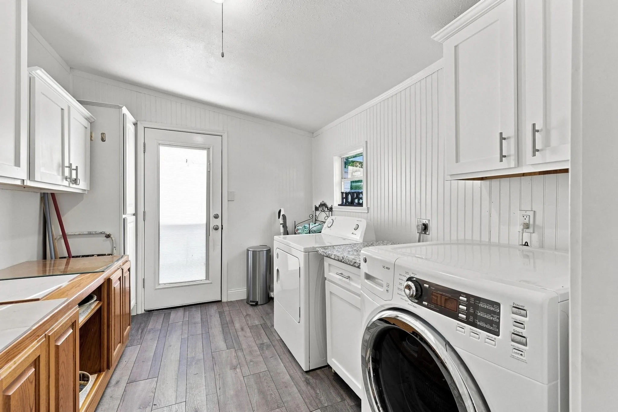 Wood-finish flooring, white beadboard wall panels, white upper cabinetry with brushed nickel hardware, and a frosted glass-paneled door