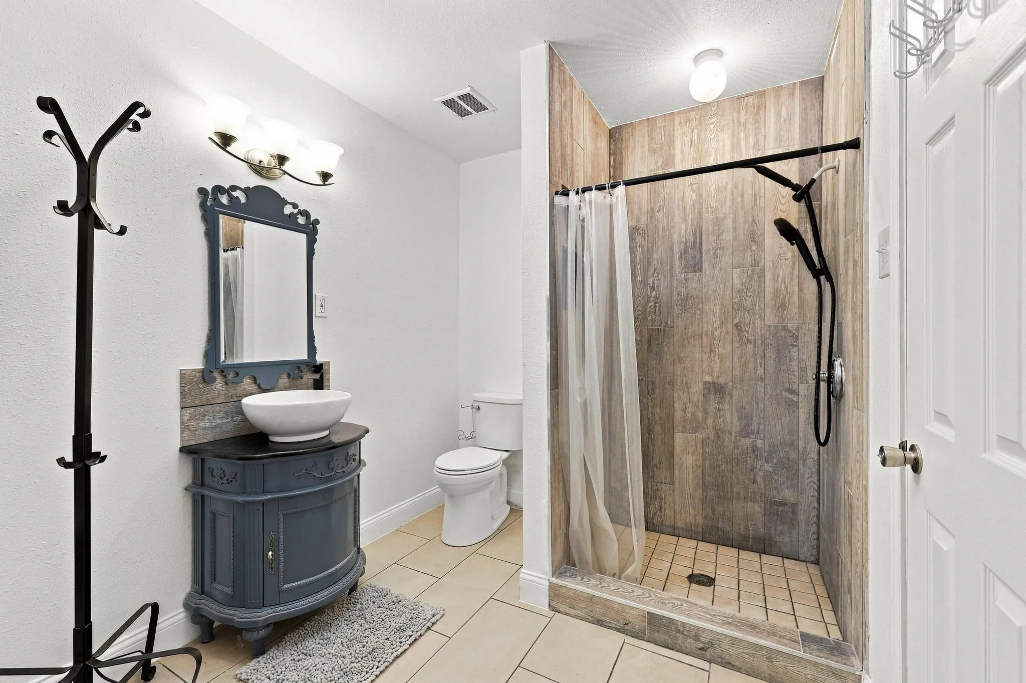 Walk-in shower with wood-finish tile surround, floor-mounted toilet, and a vanity featuring a vessel sink