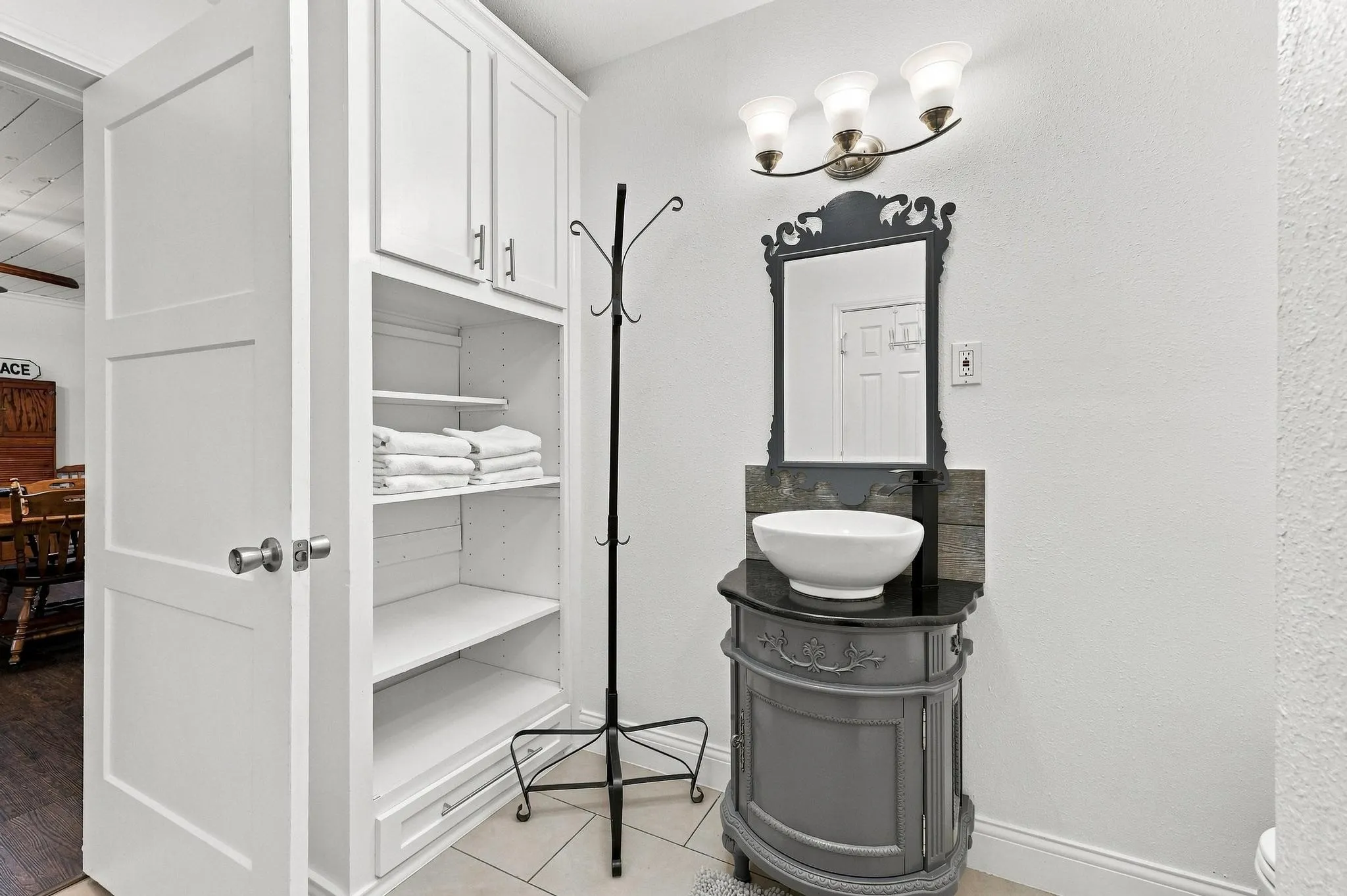 Built-in cabinetry with shelving, vanity with vessel sink, ornate mirror, and wall-mounted light fixture