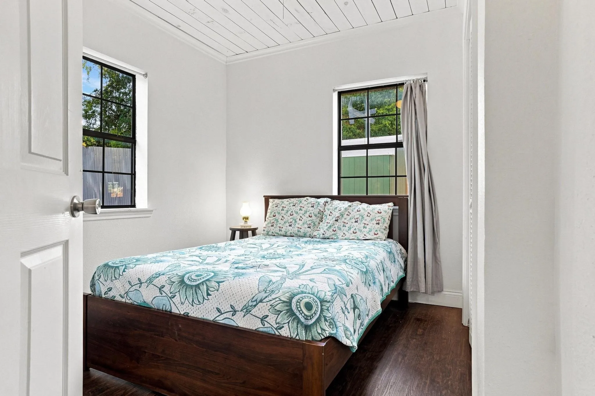 White shiplap ceiling, dark wood-finish flooring, white walls, and two windows with black grid panes