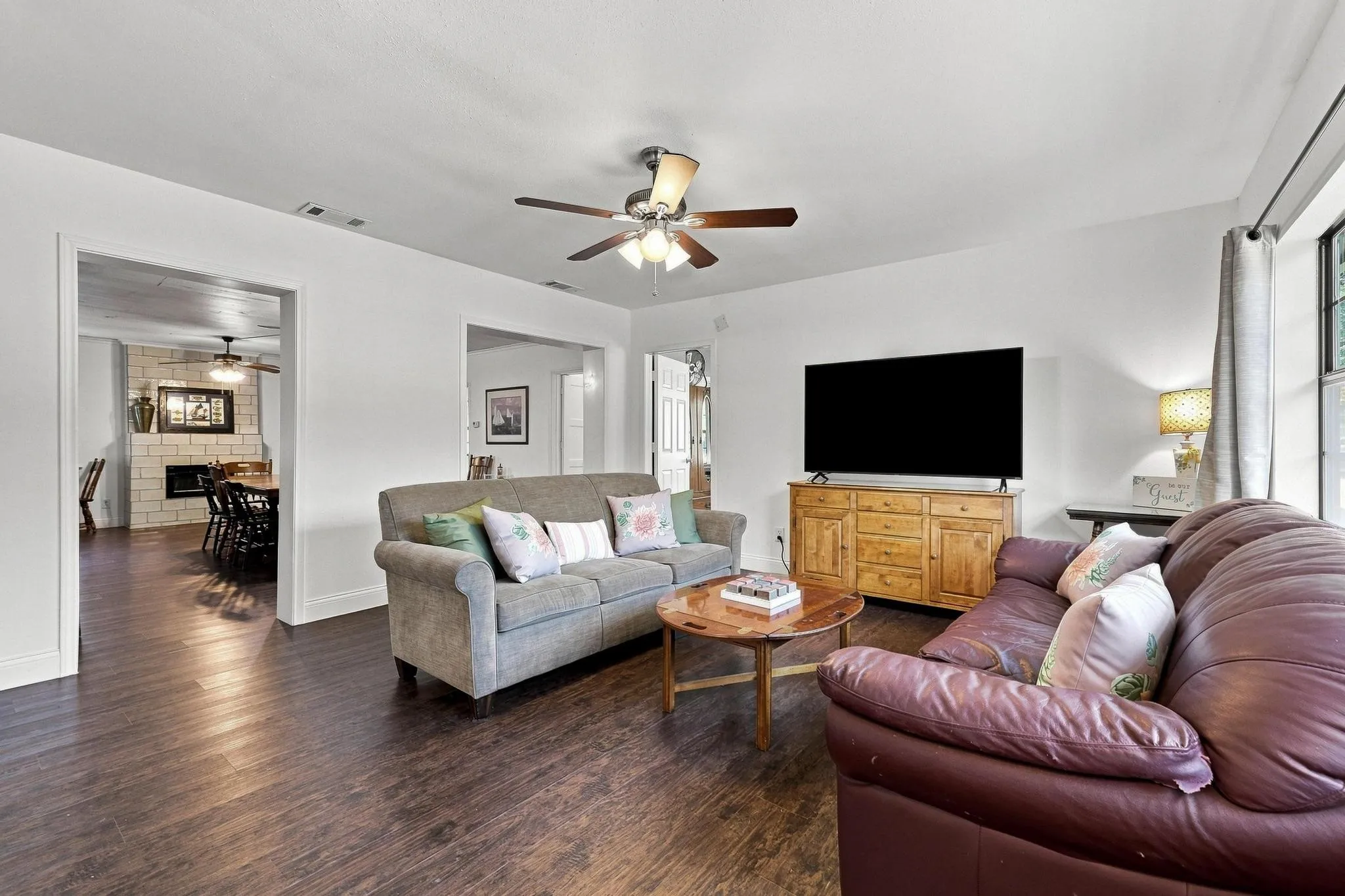 Wood-finish flooring throughout, white walls, and a ceiling fan with integrated lighting