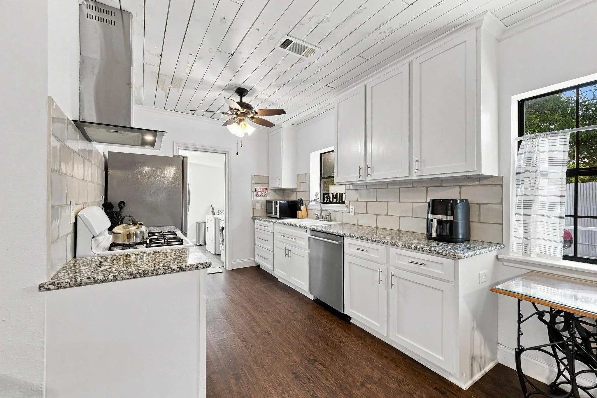 Wood-finish flooring, white cabinetry with silver-tone hardware, light-toned subway tile backsplash, and speckled countertops