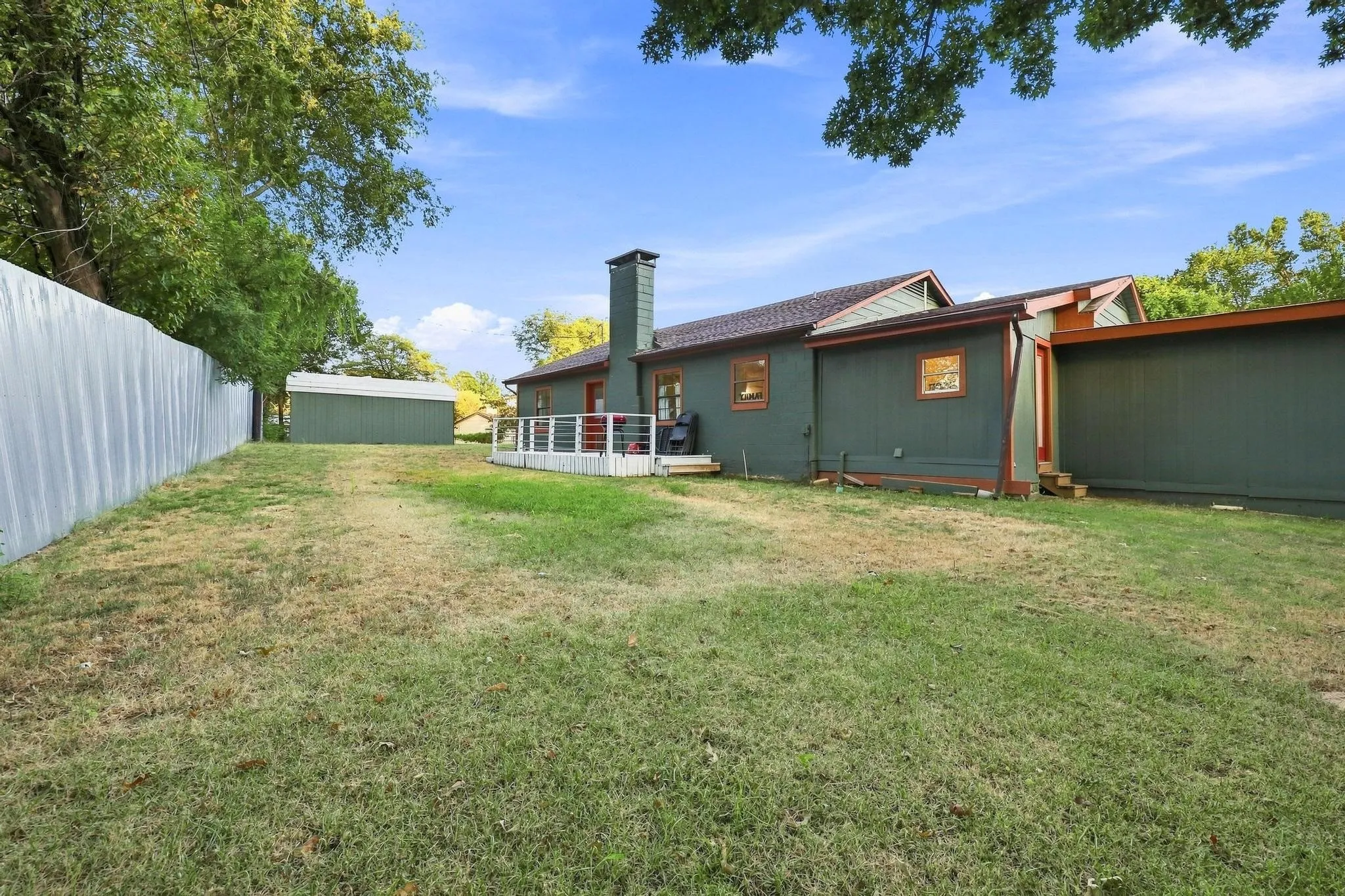 Expansive lawn featuring a storage shed, composite decking, and a corrugated metal fence
