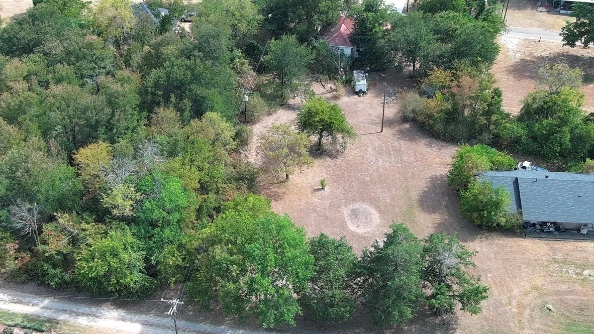 Expansive lot featuring mature trees, a partially cleared area, and a dark shingle roof structure