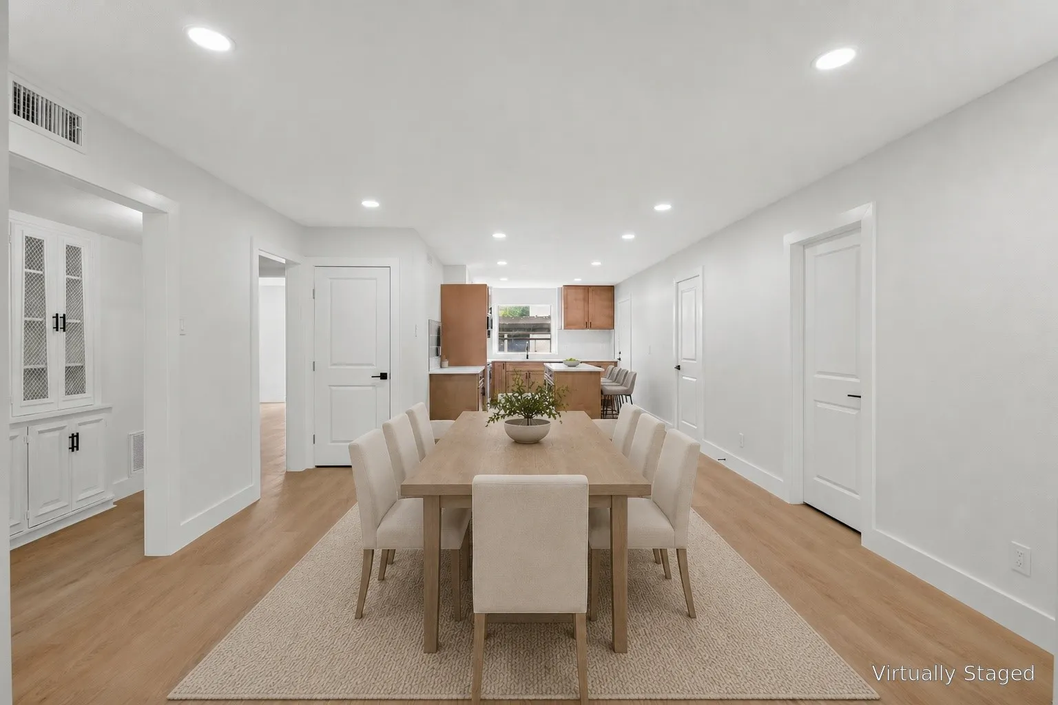 Open-concept dining and kitchen area featuring warm wood-finish flooring throughout, recessed ceiling lighting, and white shaker-style cabinetry with hardware accents