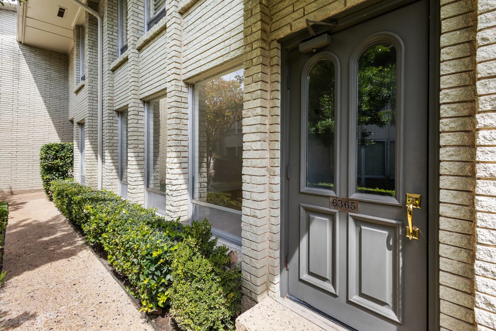 Elegant brick and stone facade with dark-framed dual-door entry featuring glass panels and brass hardware