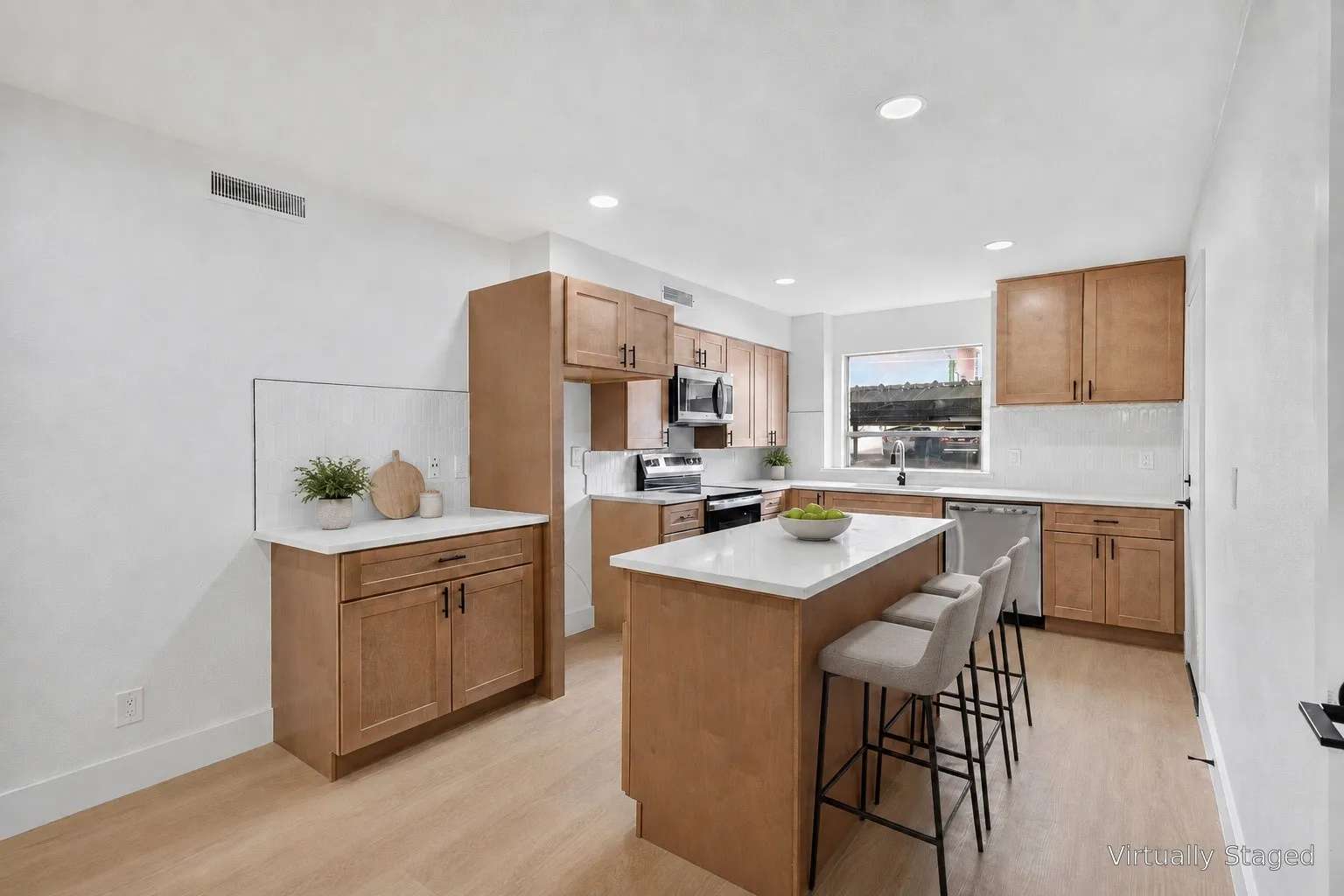 Kitchen featuring light wood-finish cabinetry, white countertops, a tiled backsplash, stainless steel appliances, and a central island with seating