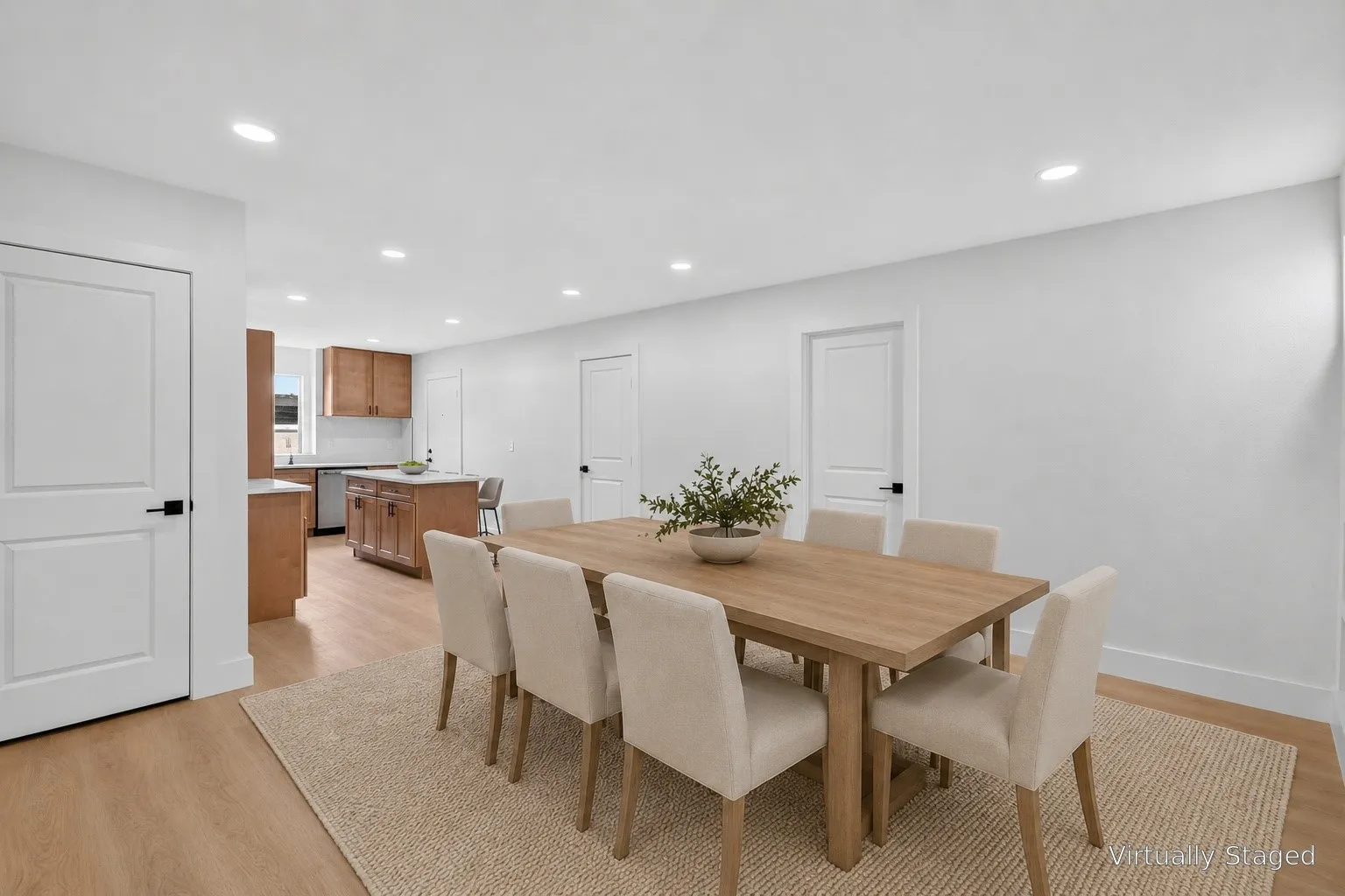 Recessed lighting illuminates the dining area with light wood-finish flooring