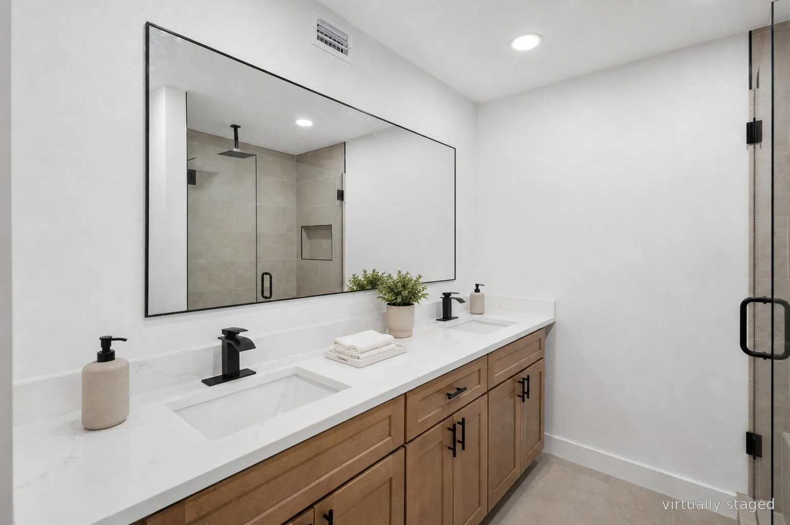 Spa-inspired primary bathroom featuring a wood-finish vanity with dual matte black faucets, white quartz countertop, and an oversized framed mirror
