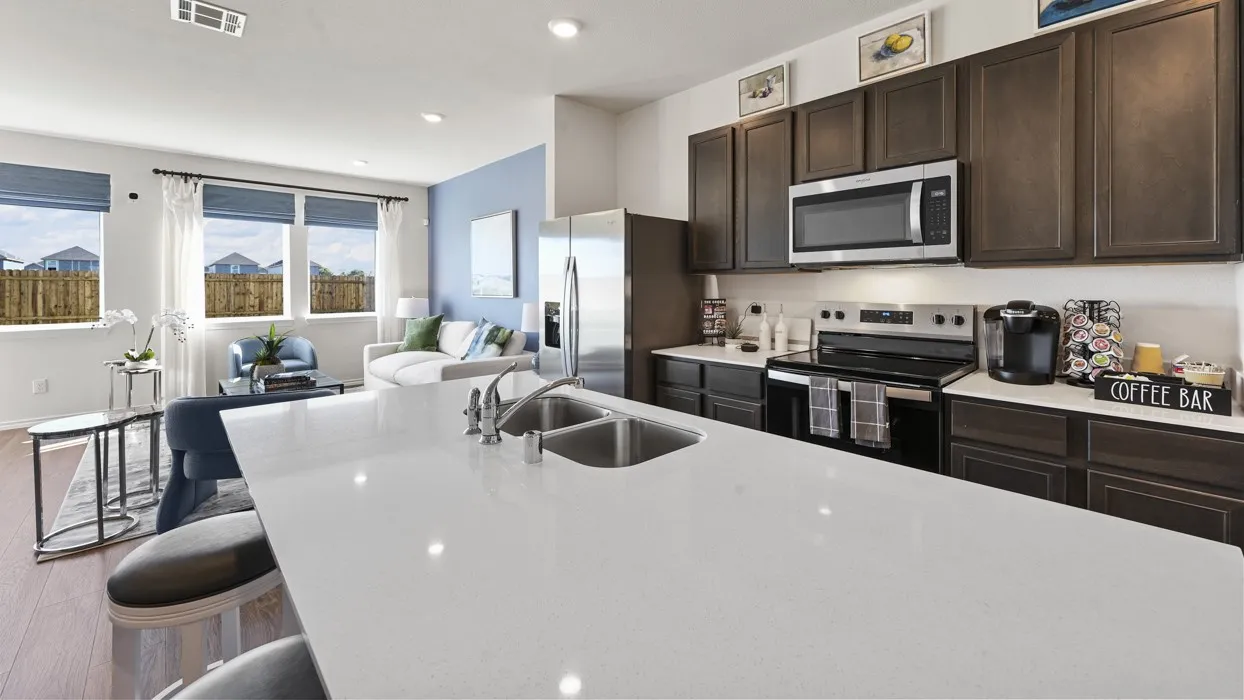 Open-concept living space featuring wood-finish flooring, a kitchen island with integrated sink, dark wood cabinetry, and stainless steel appliances