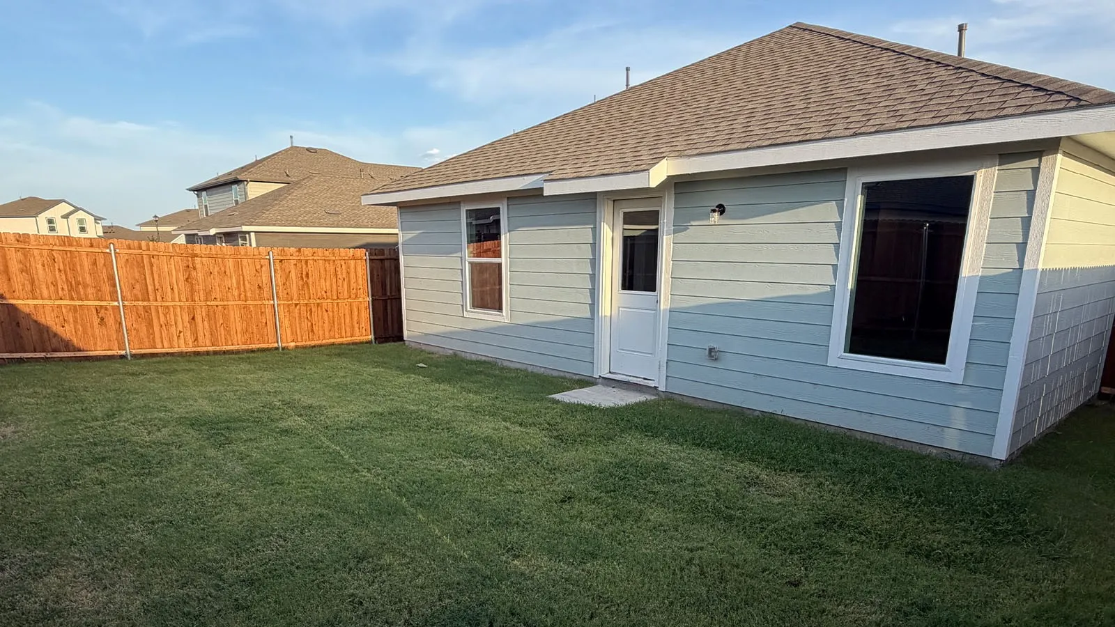 Spacious fenced yard featuring a manicured lawn, wood fencing, light blue siding, and a gabled roof