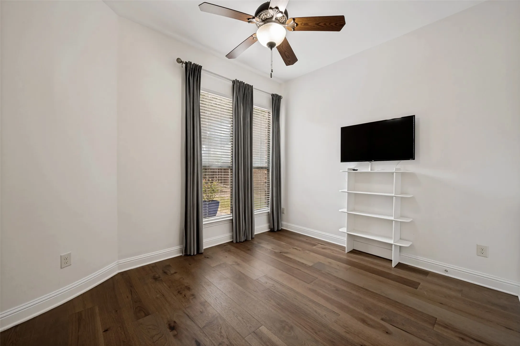 This spacious secondary bedroom offers soaring ceilings, rich hardwood floors, abundant natural light, and a ceiling fan, creating a comfortable retreat for family or guests.