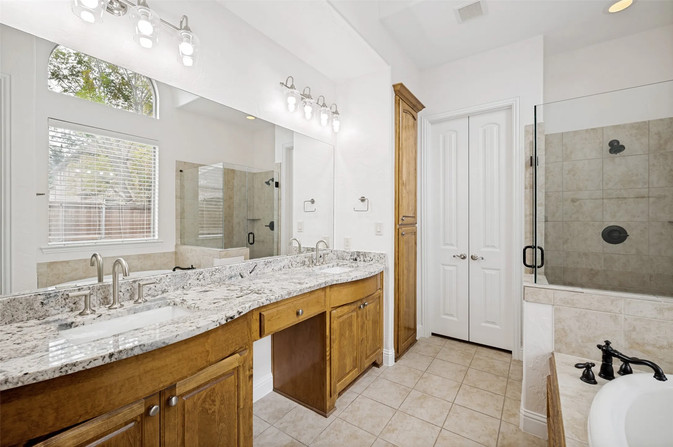 Unwind in the luxurious primary bath featuring dual granite vanities, a relaxing soaking tub, an oversized frameless glass shower, abundant storage, and a dedicated makeup vanity—creating the perfect spa-inspired retreat.