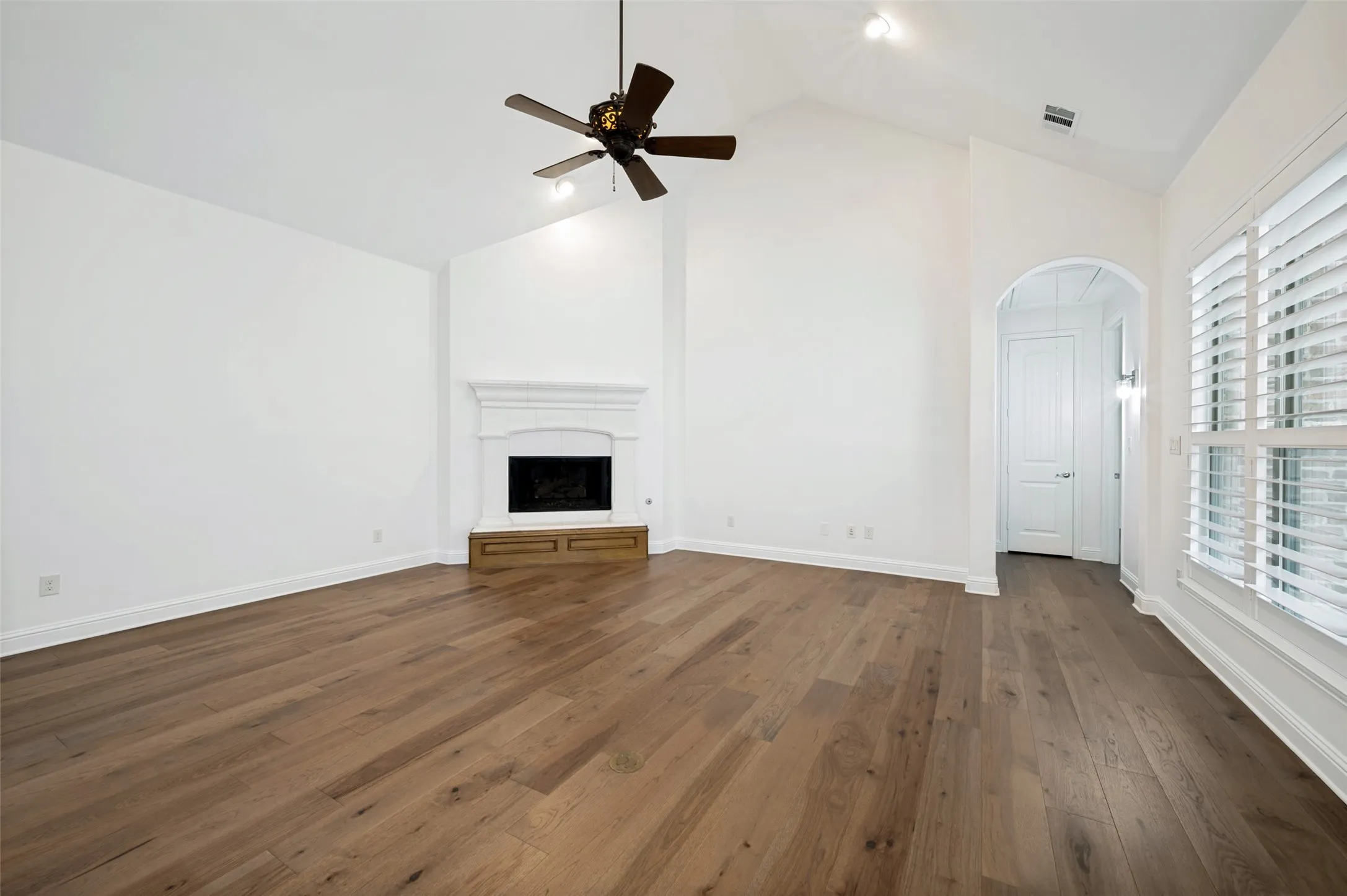 The spacious family room showcases soaring vaulted ceilings, rich hardwood floors, a beautiful cast stone fireplace, and expansive windows with plantation shutters, creating a warm and inviting space for relaxing or entertaining.