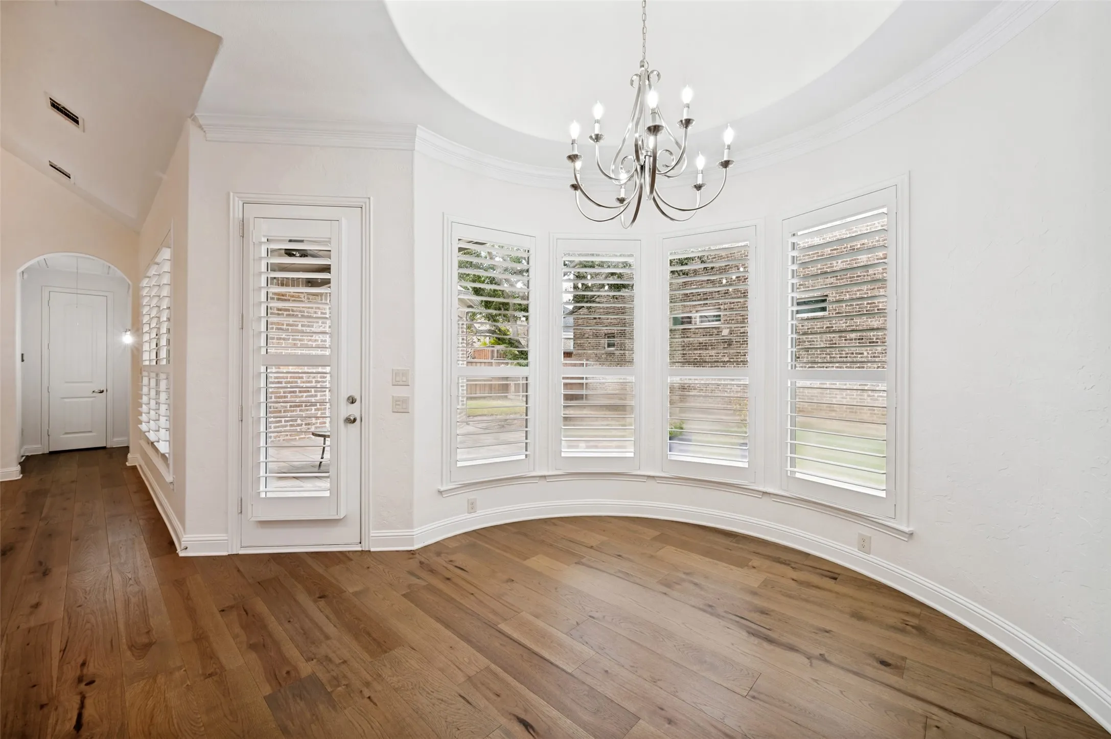 Enjoy your morning coffee in this light-filled dining space, featuring a dramatic tray ceiling, elegant chandelier, plantation shutters, and a wall of windows that fill the space with natural light.