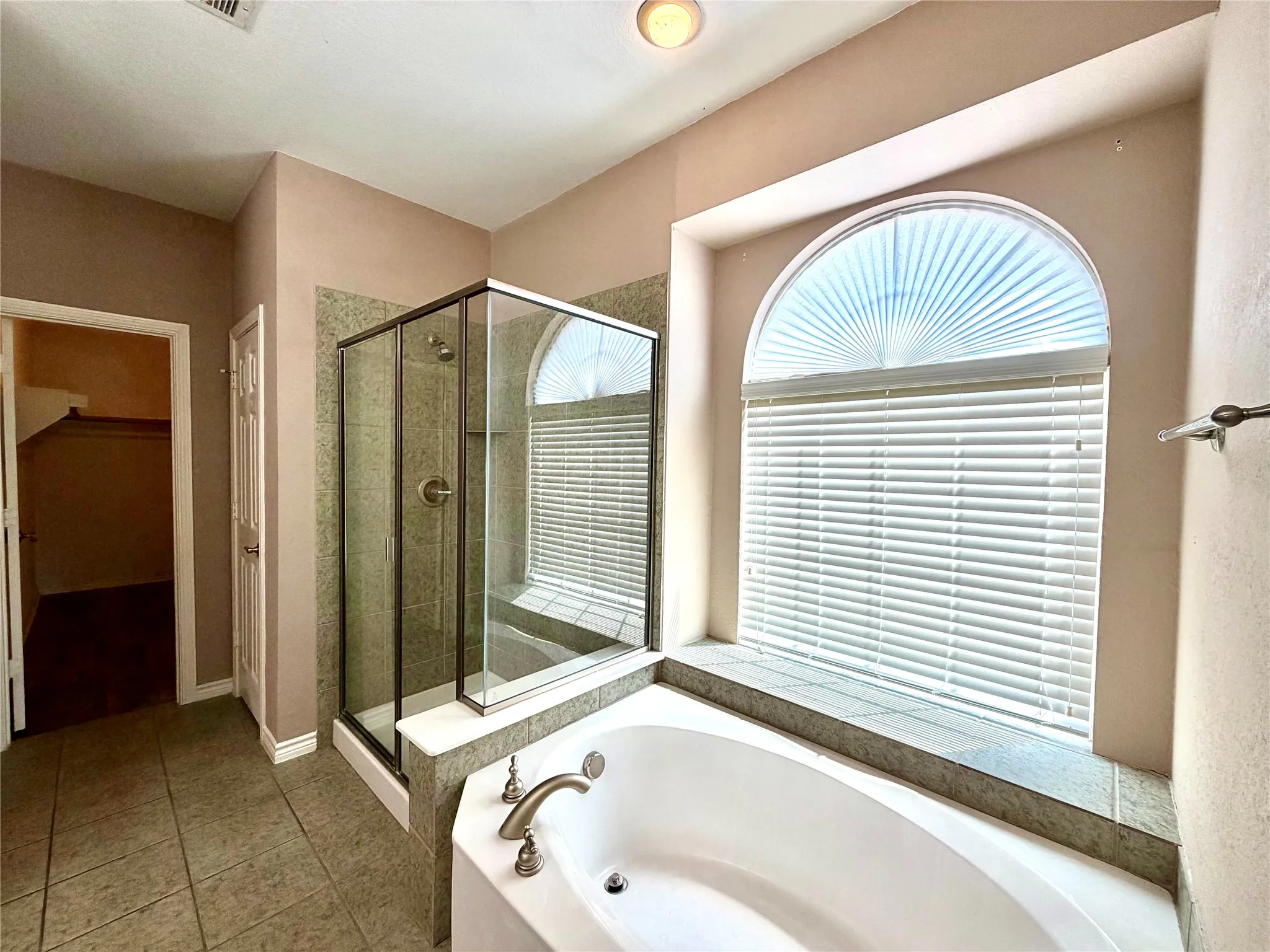 Corner soaking tub with brushed nickel fixtures, tiled surround, and arched window