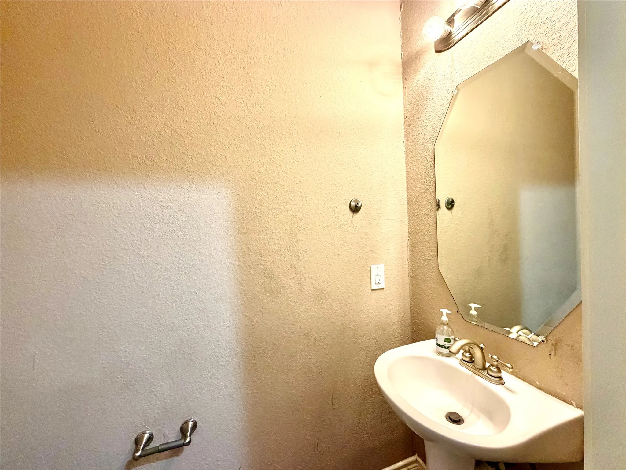 Pedestal sink with a brushed nickel faucet, an octagonal mirror, and wall-mounted lighting