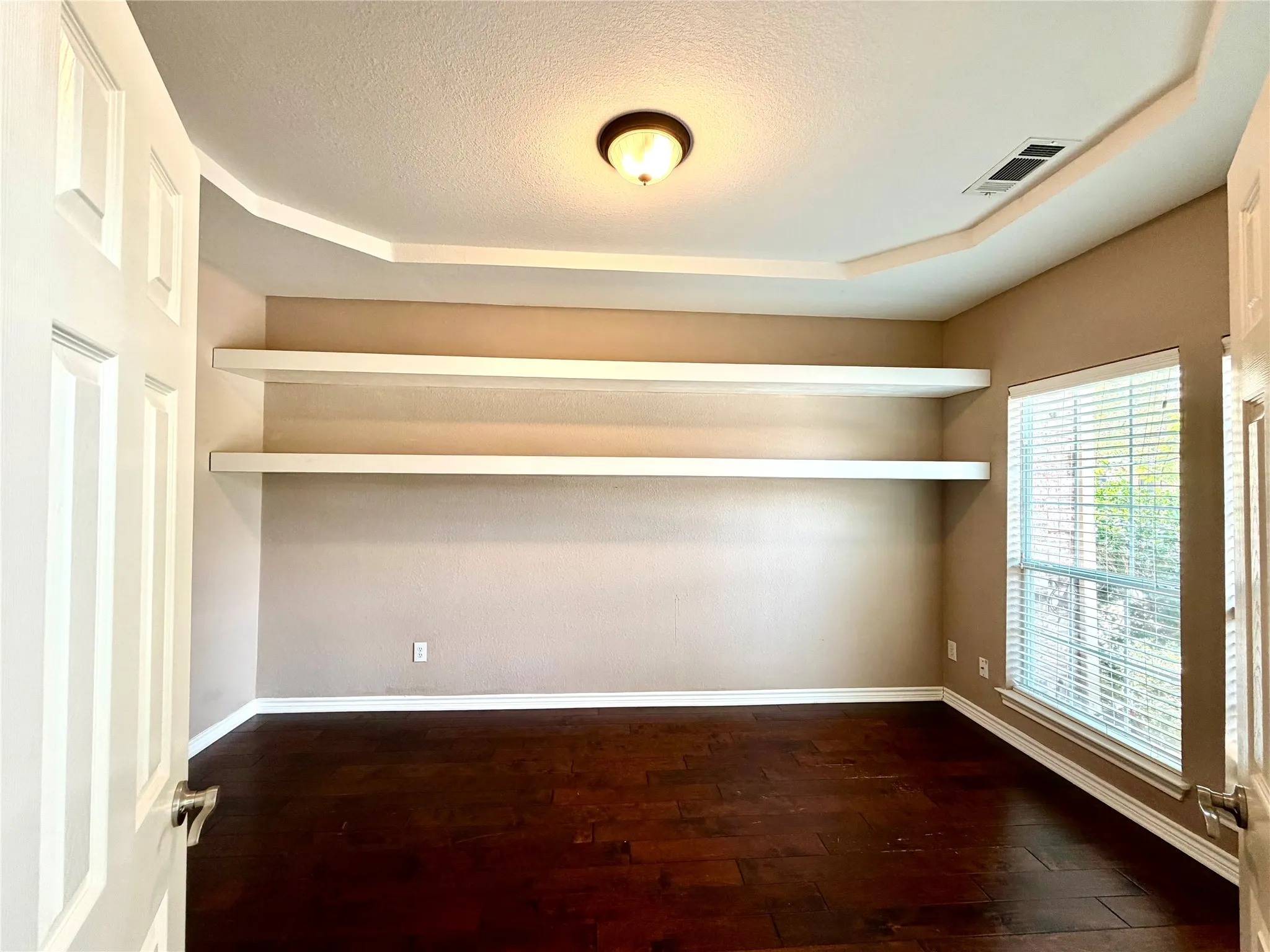 Dark wood-finish flooring with built-in shelving and a tray ceiling