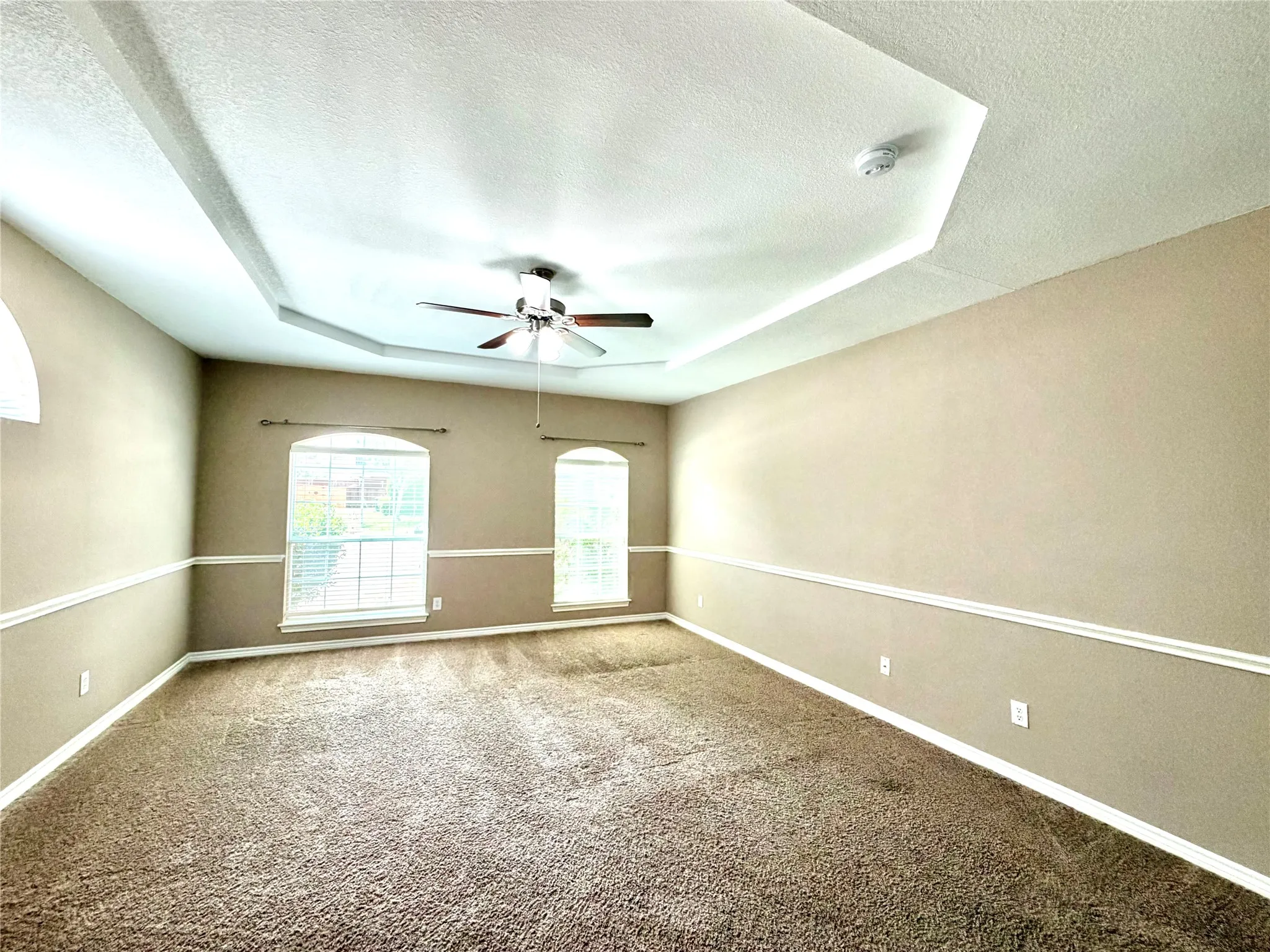 Tray ceiling with integrated lighting, ceiling fan, arched windows, and crown molding