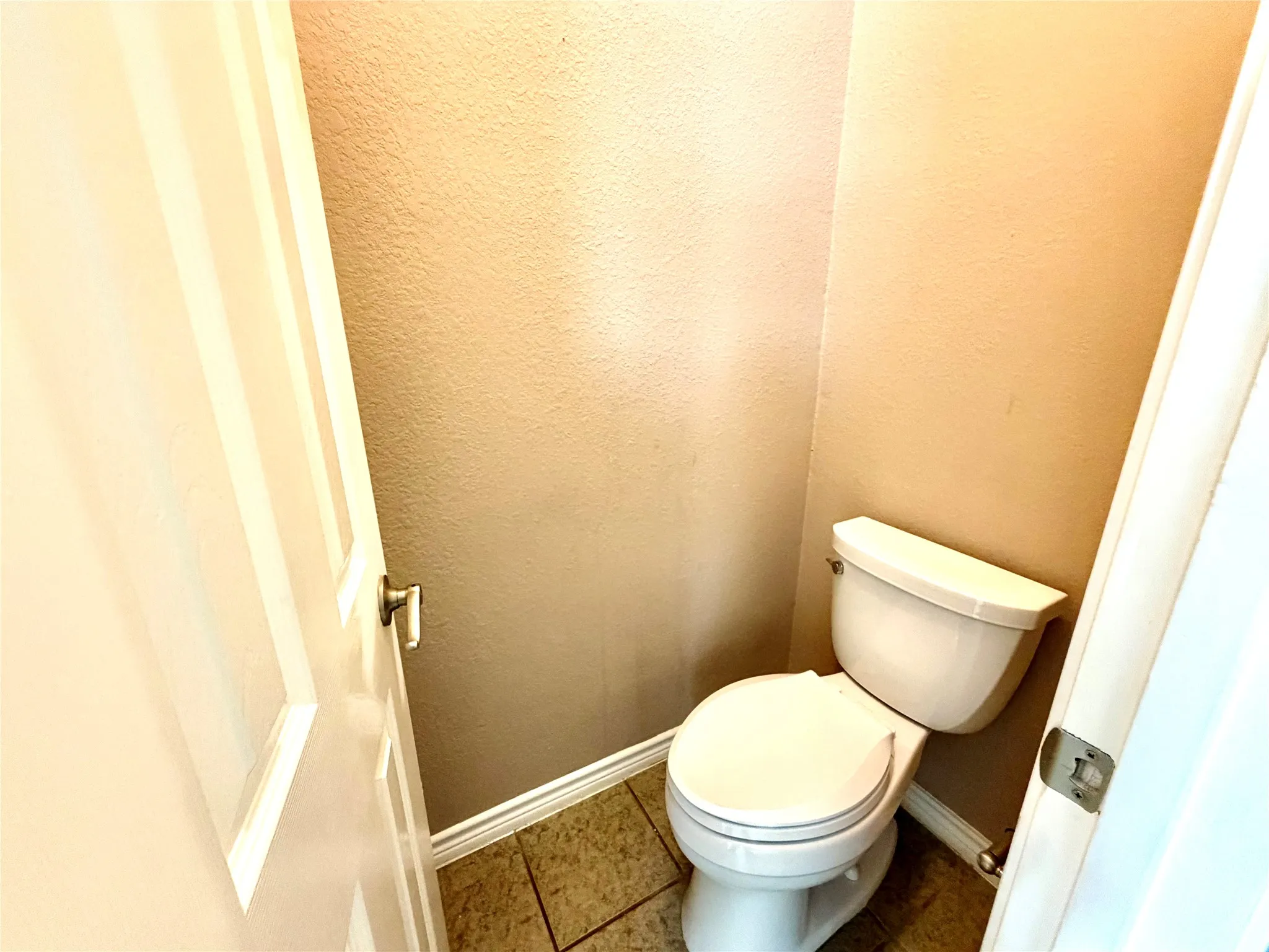 White toilet with a matching tank, set against textured walls, and complemented by tiled flooring