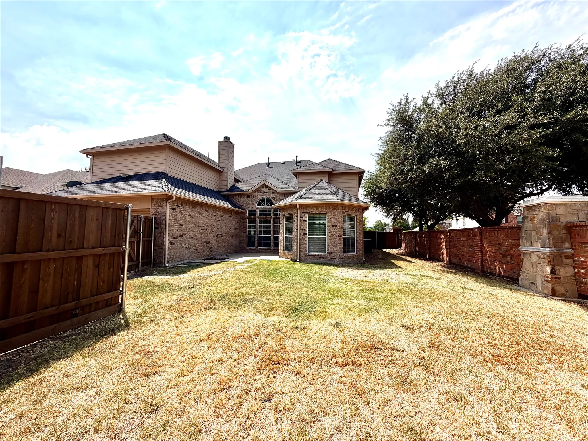 Brick exterior with multiple gables, a large mature tree, wood fencing, and a brick privacy wall