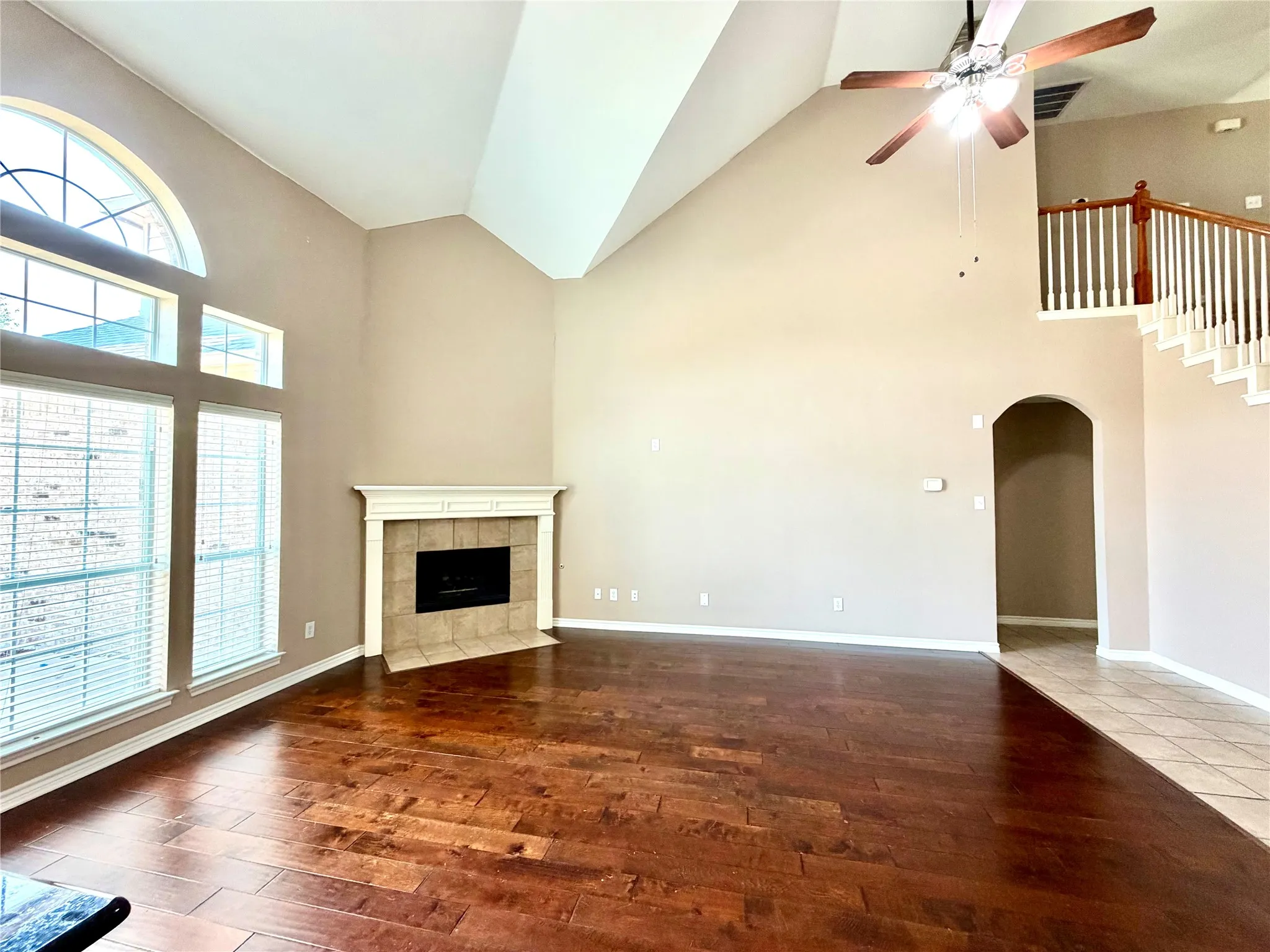 Vaulted ceiling with an installed ceiling fan, wood-finish flooring, and a fireplace with a mantel