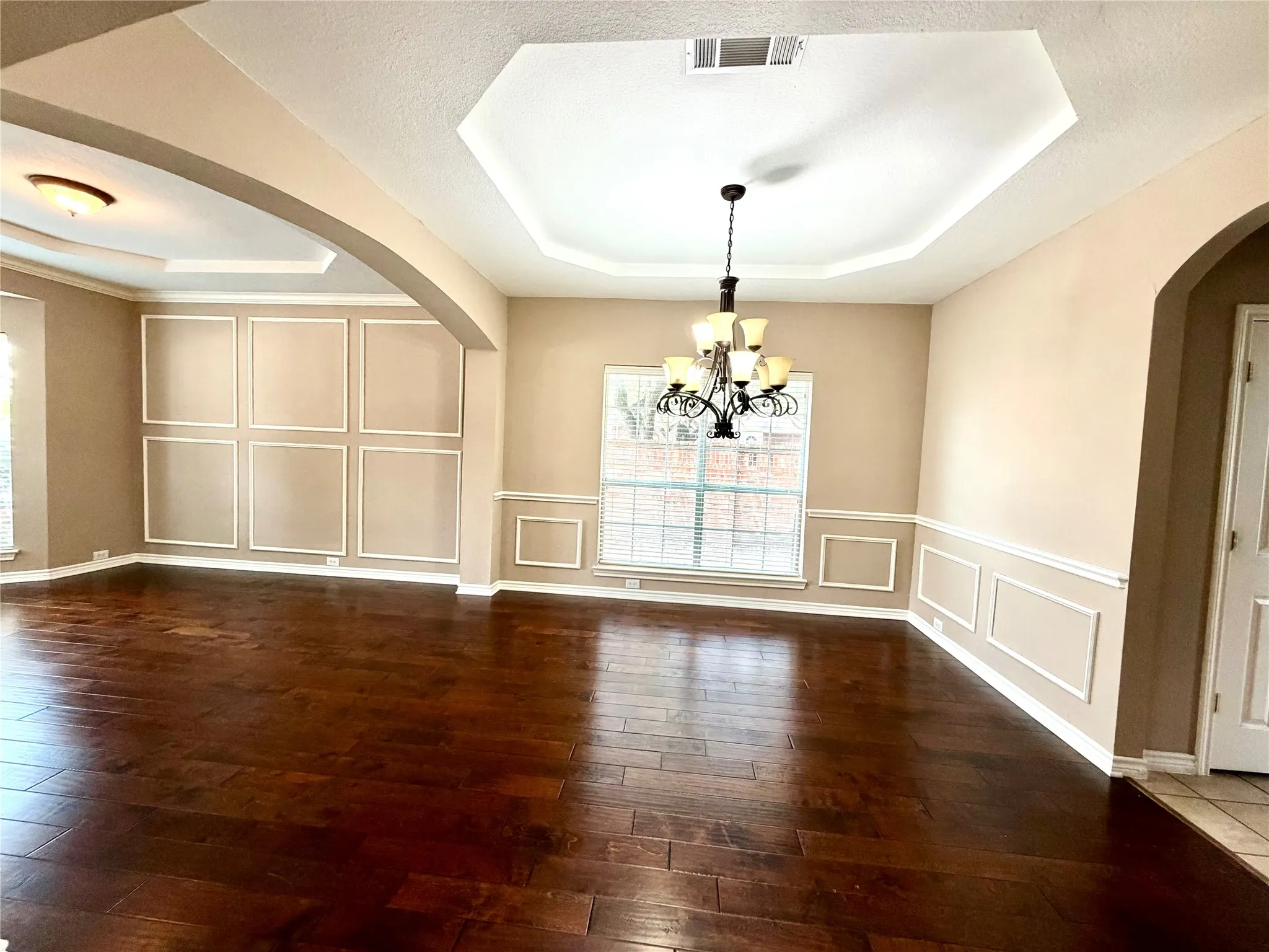 Wood-finish flooring throughout, tray ceilings, decorative wall molding, and an ornate chandelier