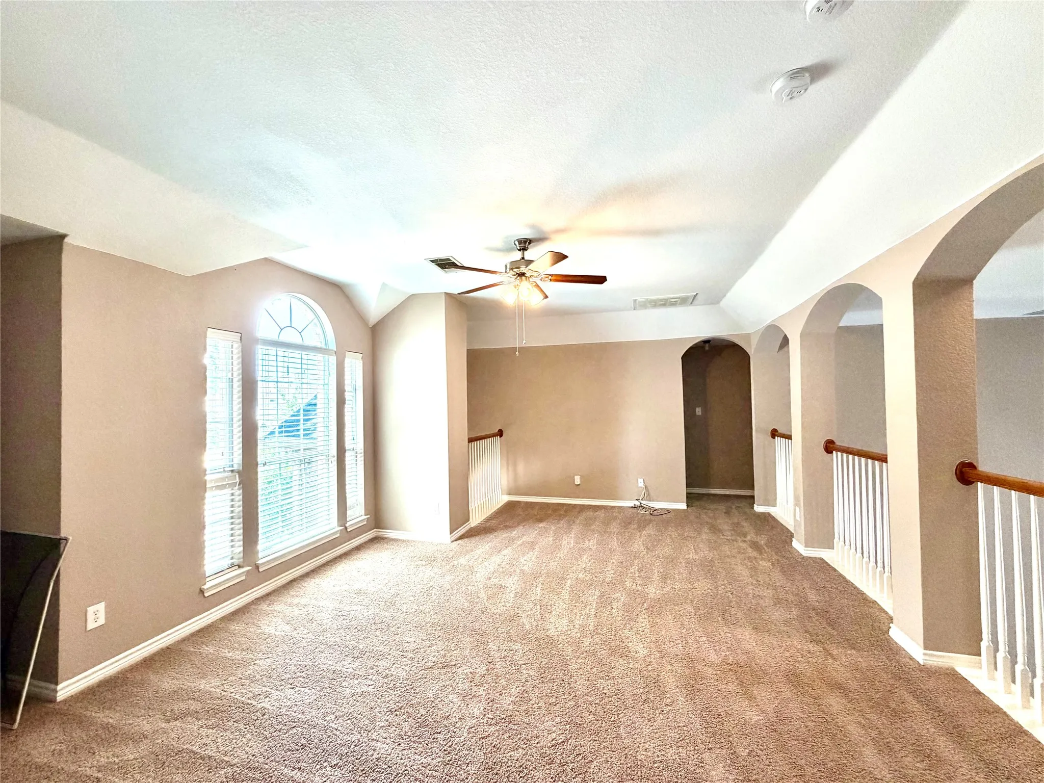 Spacious room with vaulted ceilings, arched architectural details, and carpet flooring