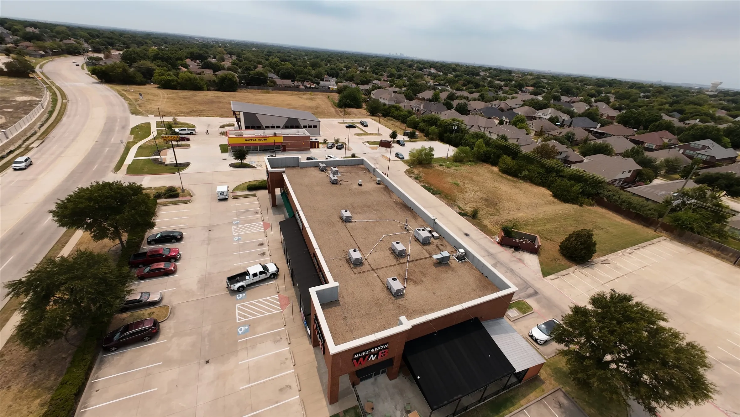 Commercial property featuring extensive paved parking, adjacent road access, and multiple air conditioning units on the roof