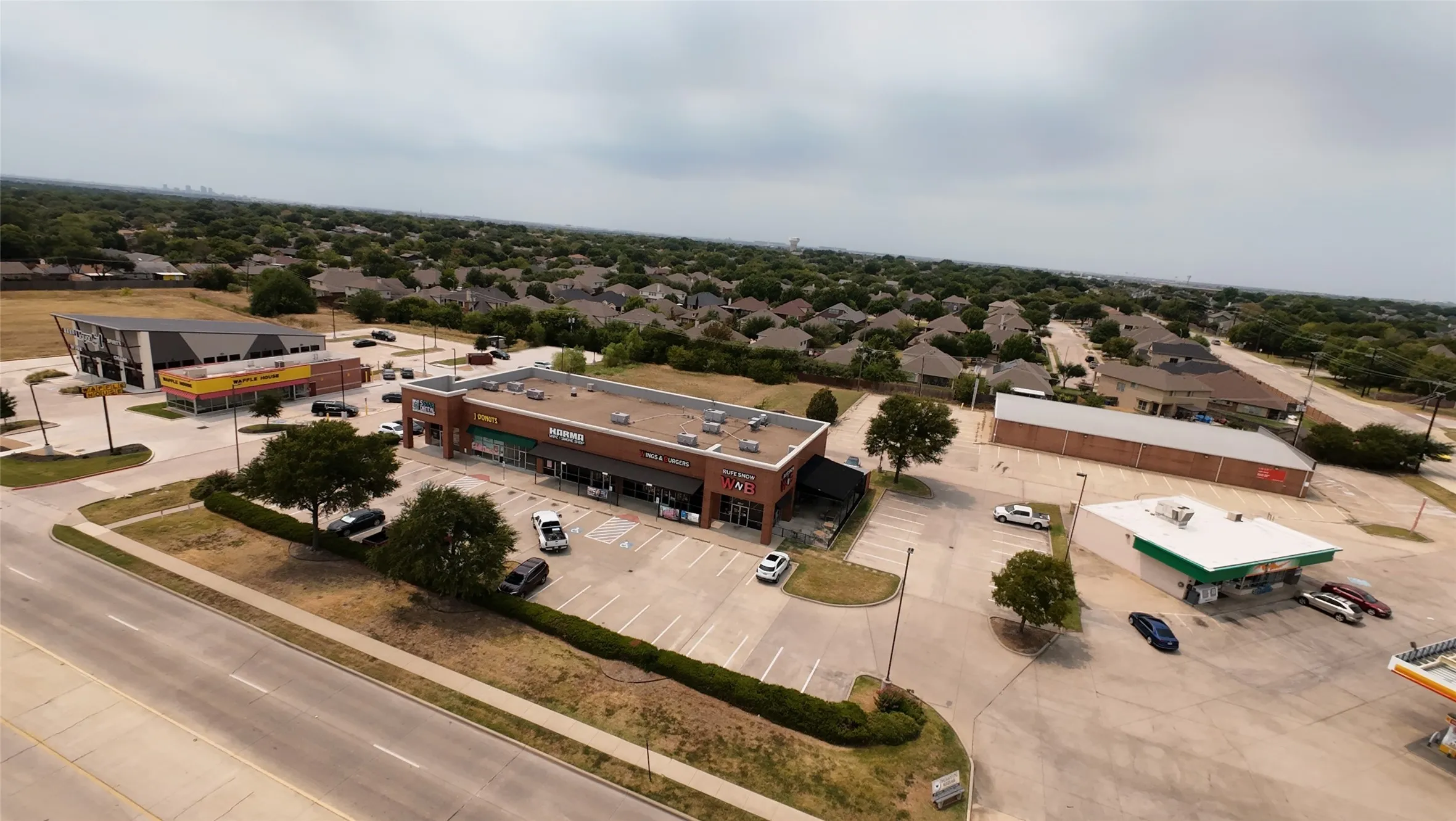 Commercial complex with multiple retail storefronts, extensive surface parking, and a prominent roadside location