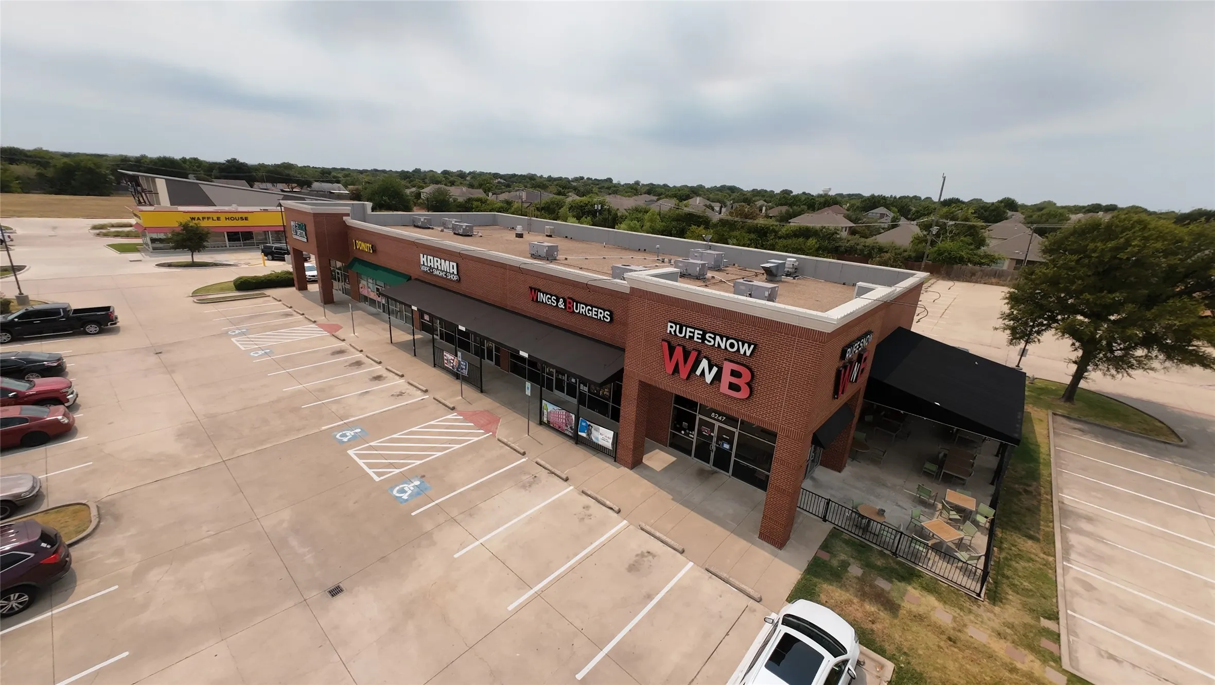 Brick facade commercial building with multiple storefronts, ample paved parking, covered outdoor patio seating, and visible signage opportunities