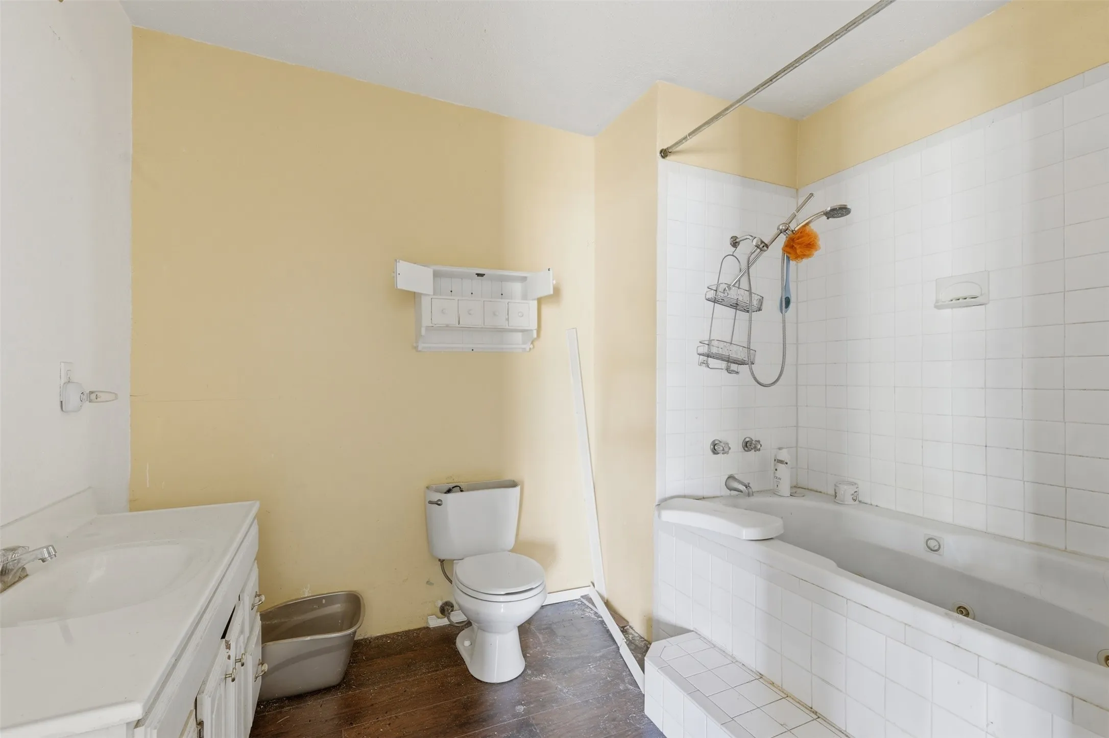 White vanity with integrated sink, white tiled tub surround, and white toilet