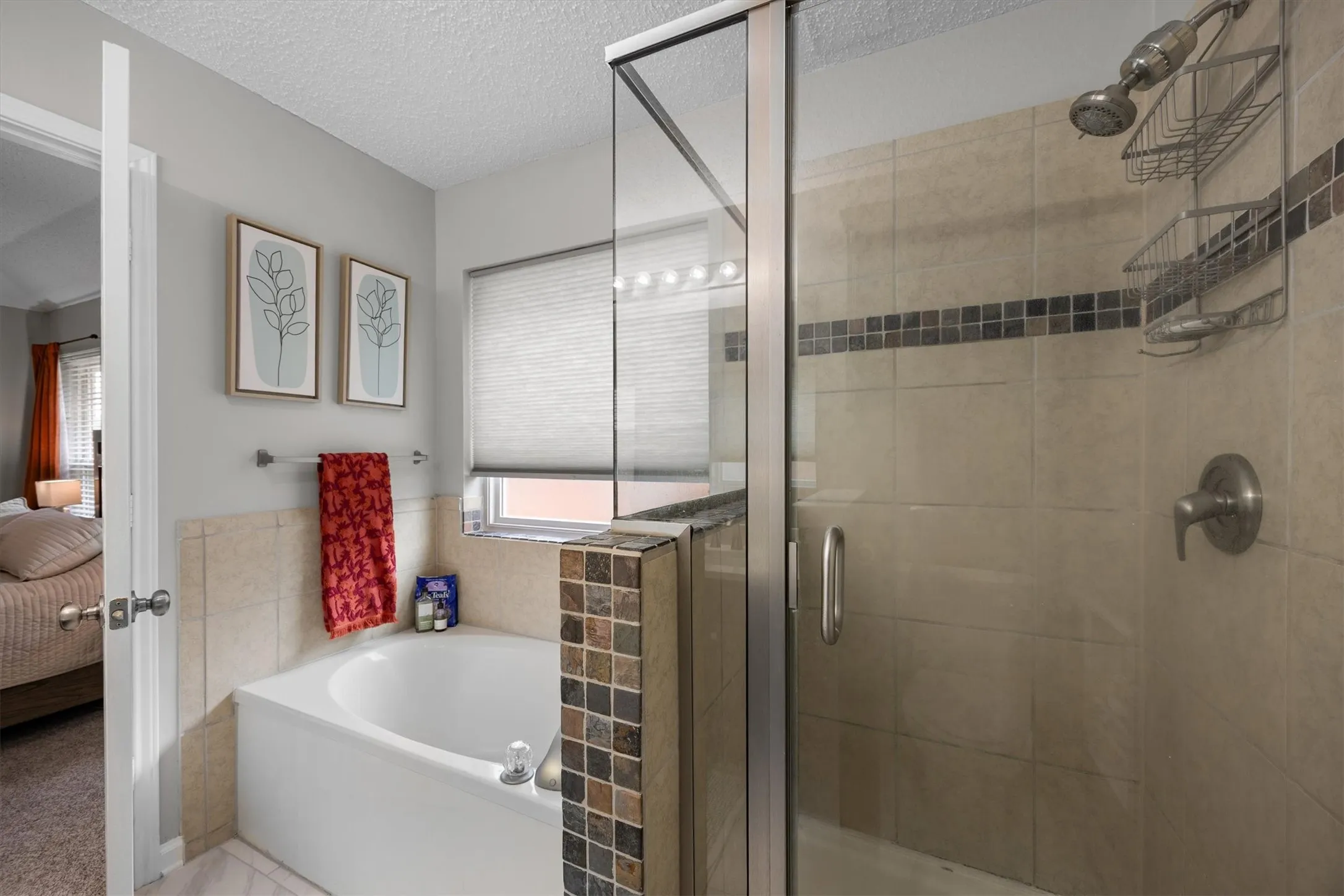 Enclosed shower with glass door and decorative tile inlay, alongside a built-in bathtub, and a window with privacy blind
