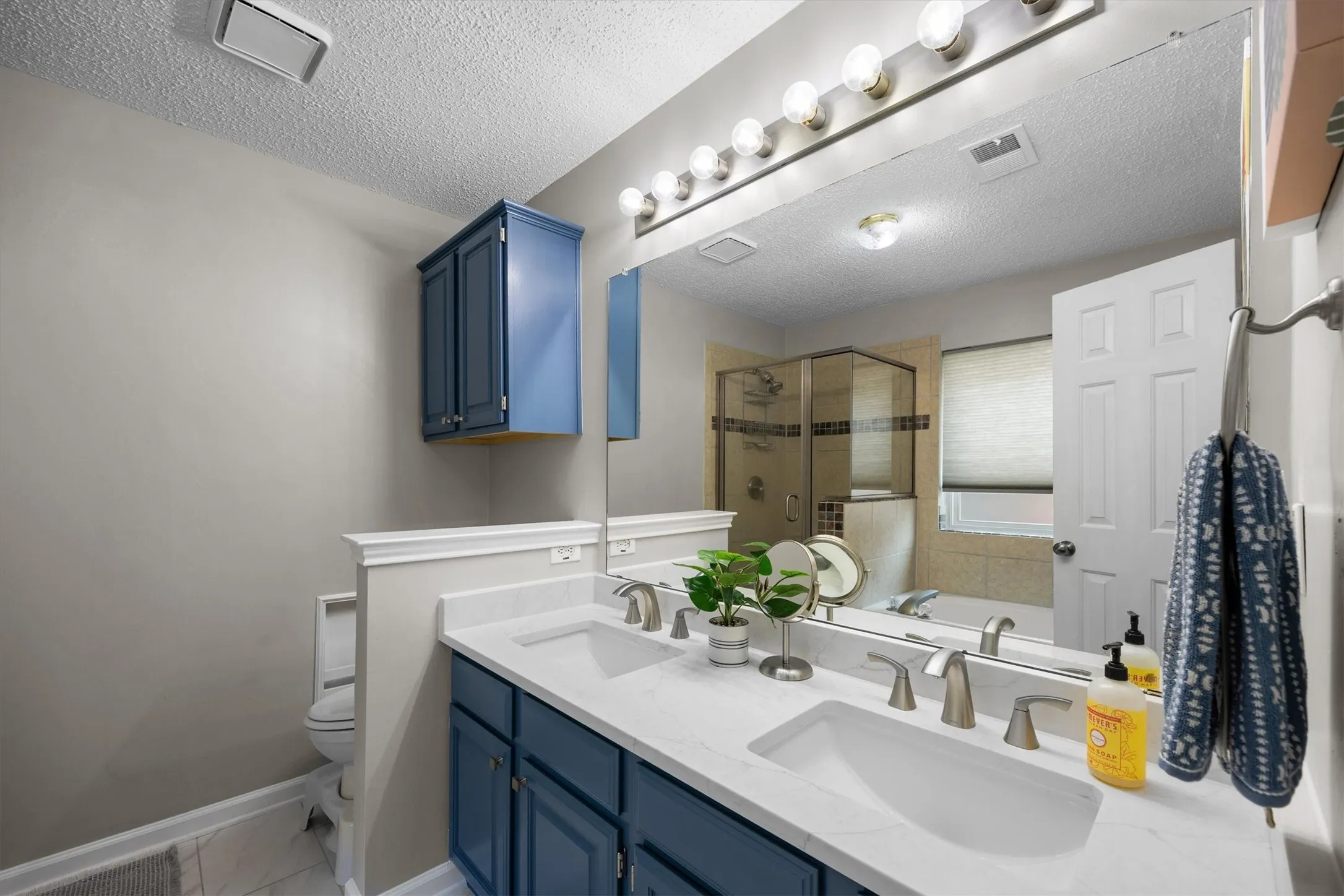 Dual vanity with undermount sinks, brushed nickel fixtures, quartz countertops and blue cabinetry gives this space a fresh modern look.