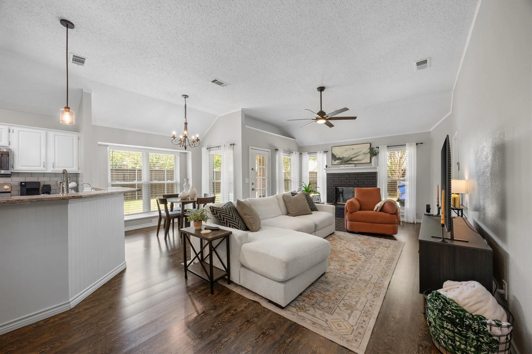 Open-concept living area featuring hardwood-like flooring throughout, abundant natural light from multiple  windows, decorative lighting, and ceiling fan.