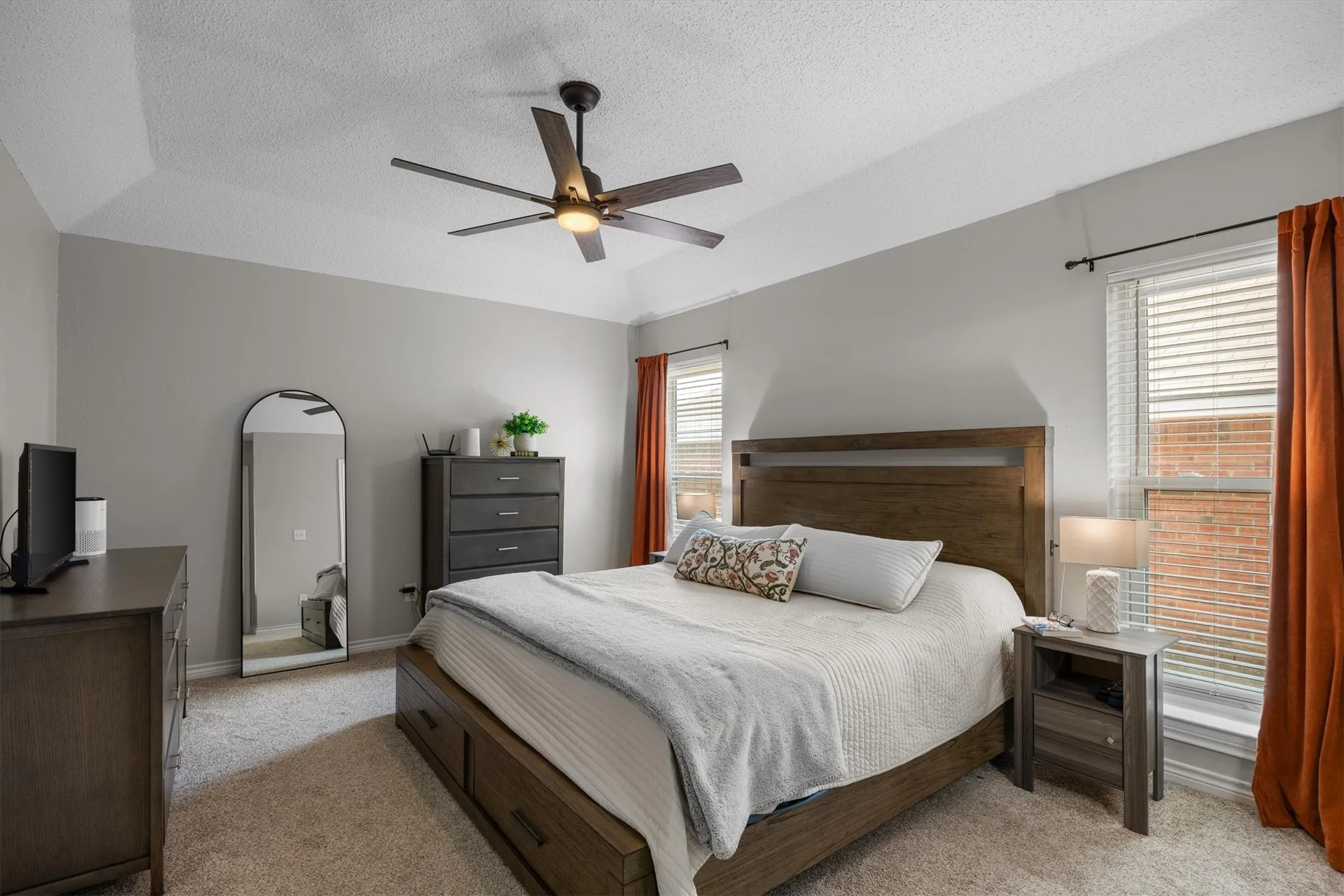 Primary bedroom offers privacy with tray ceiling with a ceiling fan, wall-to-wall carpeting, and multiple windows with blinds