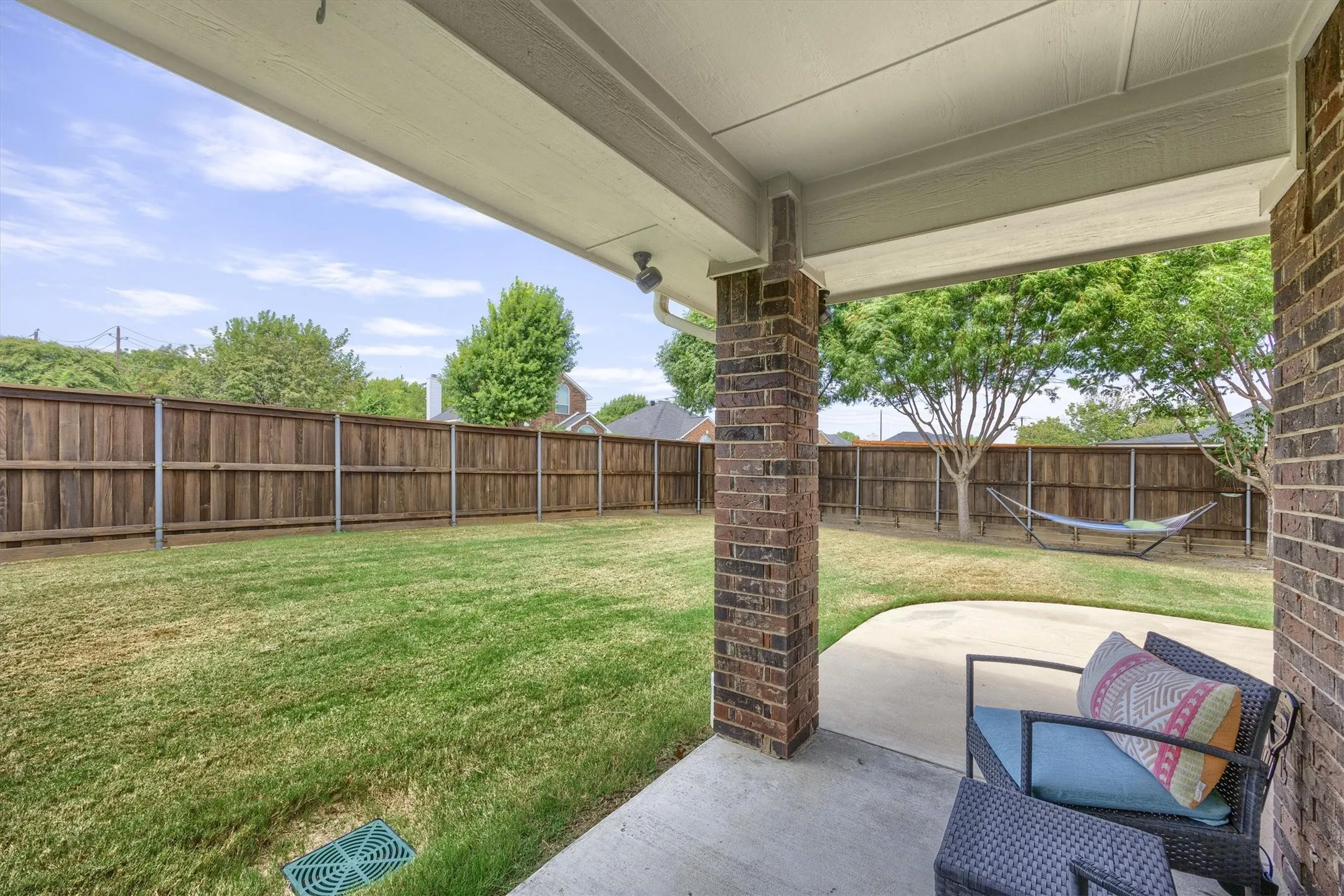 Expansive backyard featuring a manicured lawn, full privacy fencing, and a covered concrete patio