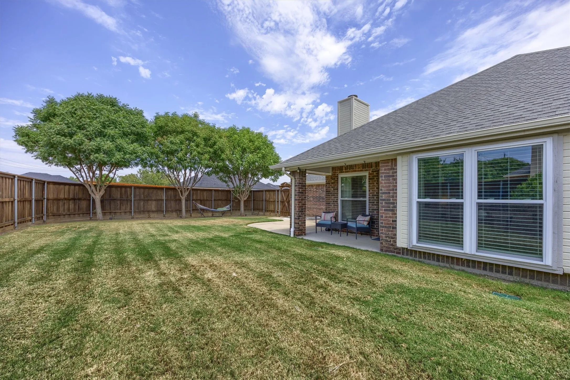 Expansive backyard featuring a manicured lawn, mature shade trees, and wooden privacy fencing