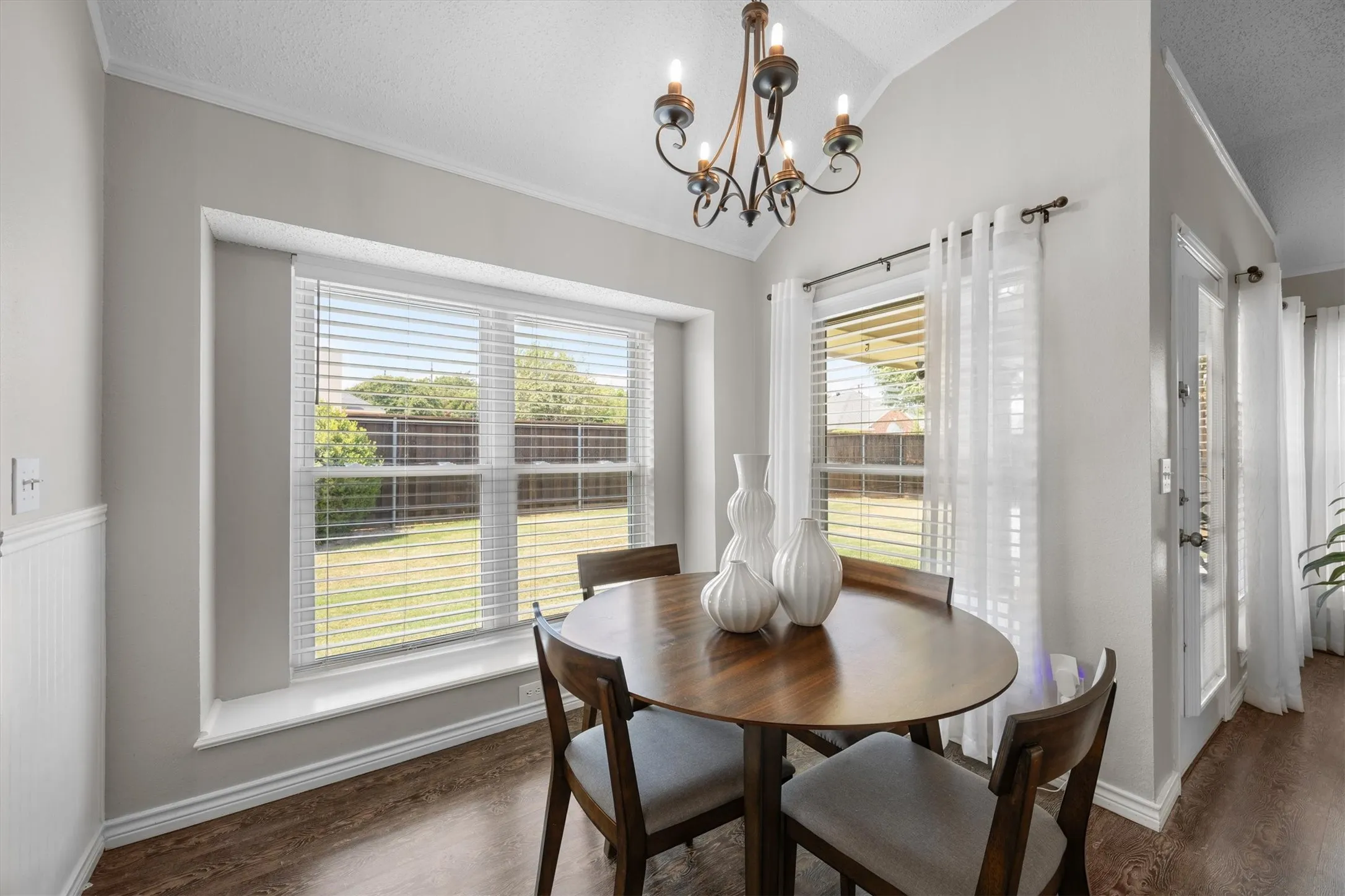 High ceiling with an iron chandelier, wood-finish flooring, and a large window overlooking the backyard