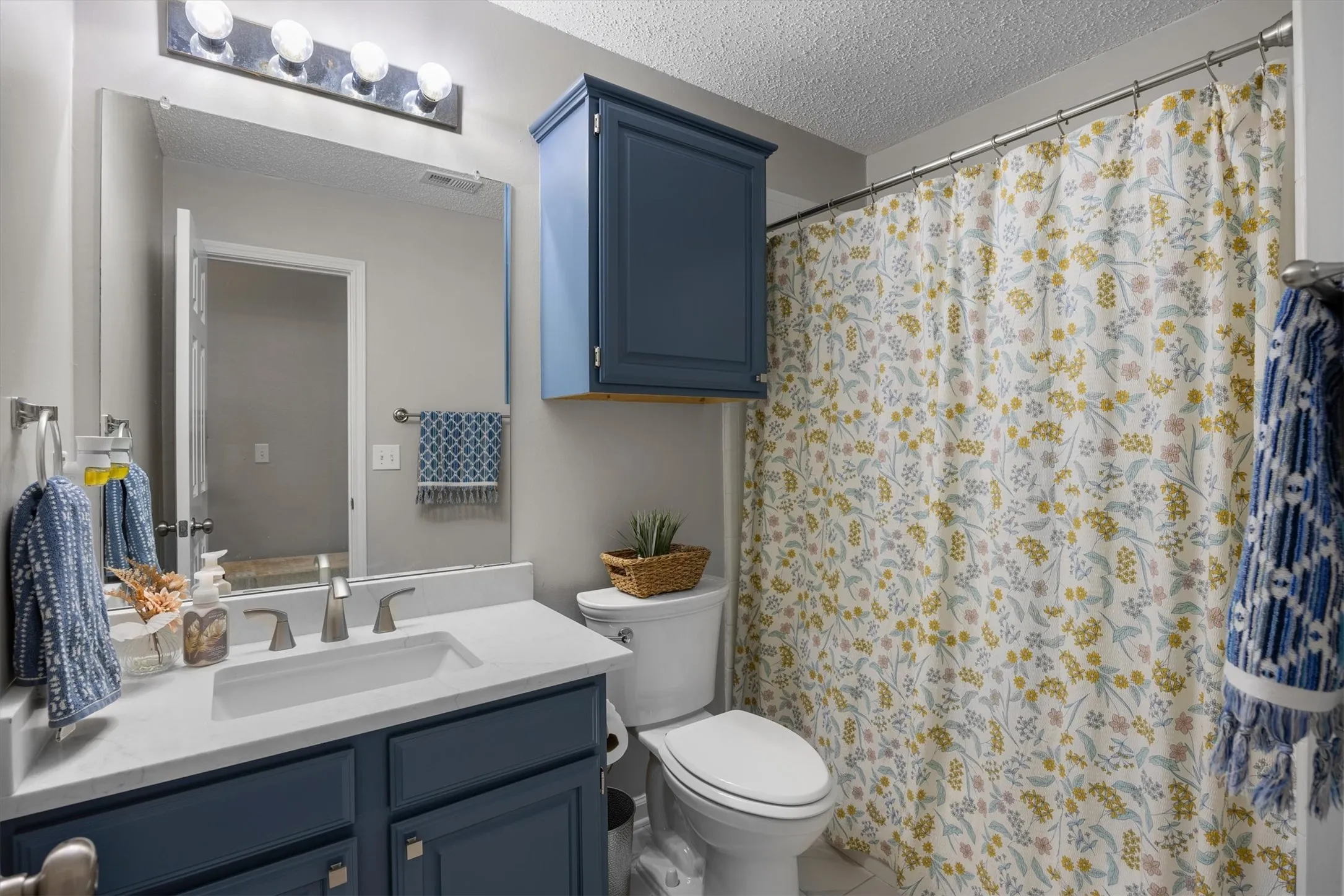 Newly renovated bath with quartz countertop and integrated sink, dark blue cabinetry, wall-mounted mirror, and overhead lighting. Looks like a model home.